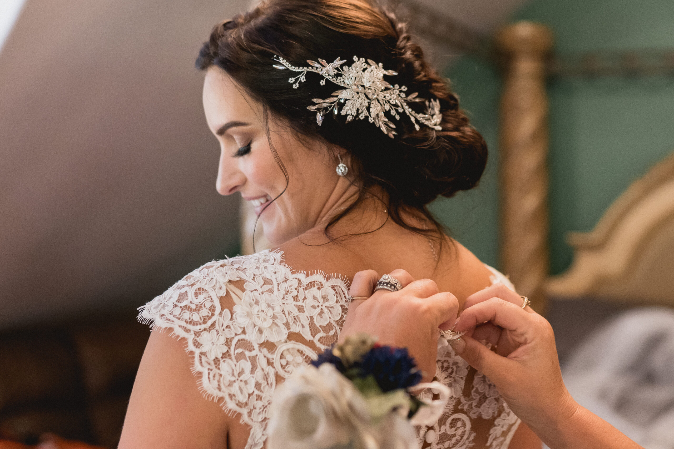 Bride smiling looking over shoulder, with her dark hair held back by a sparkling wedding comb, her wedding dress being done up