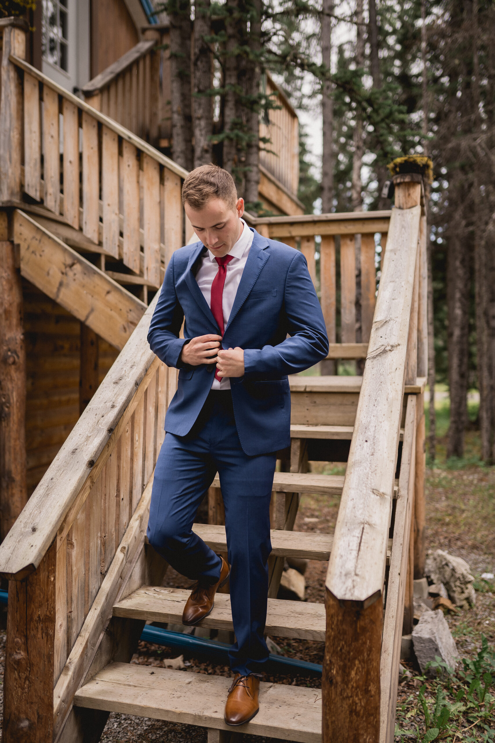 Groom in a blue suit with a red tie walking down stairs towards his wedding