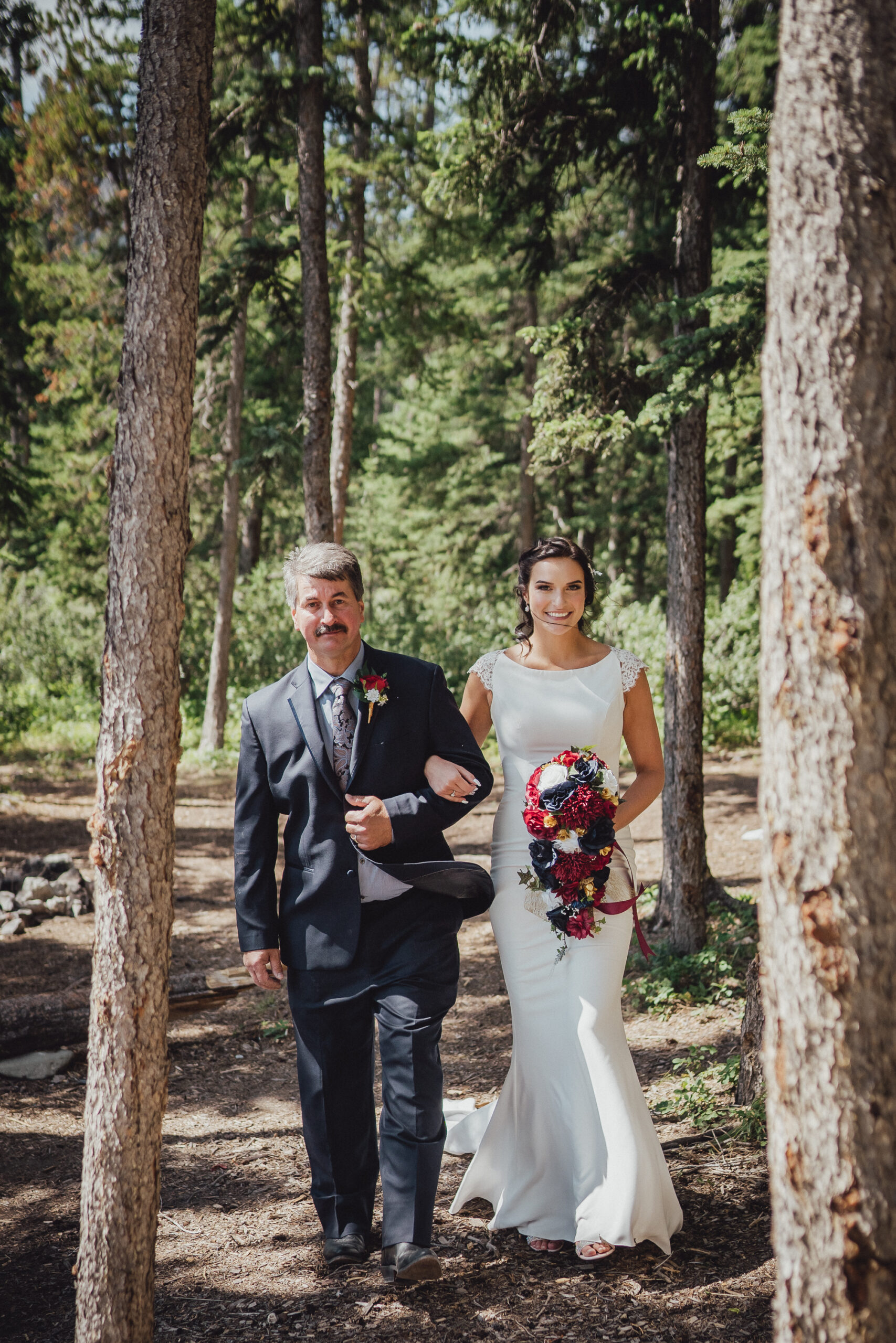 Classic bride in high neck wedding gown walking down the aisle through the woods, with her father