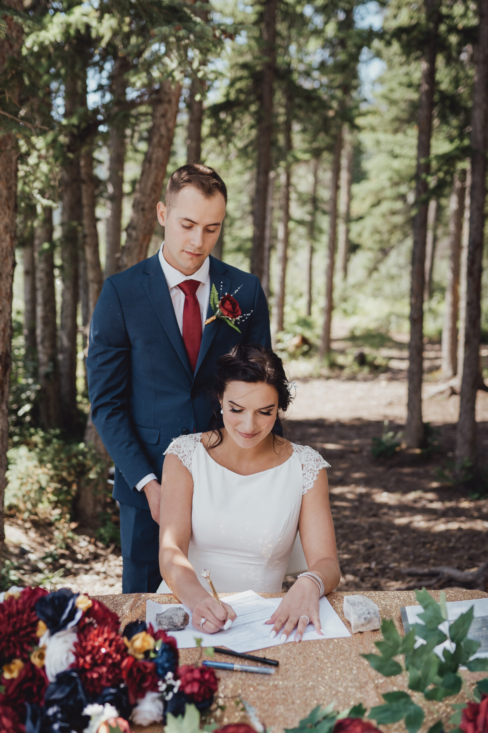 Couple in the woods signing their wedding license with red wedding flowers in the foreground