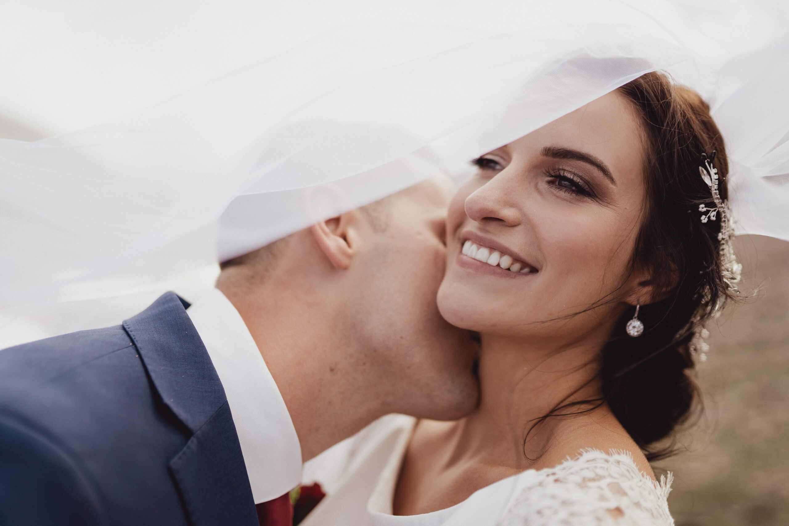 Bride and groom smiling and kissing with veil flowing in front of her face