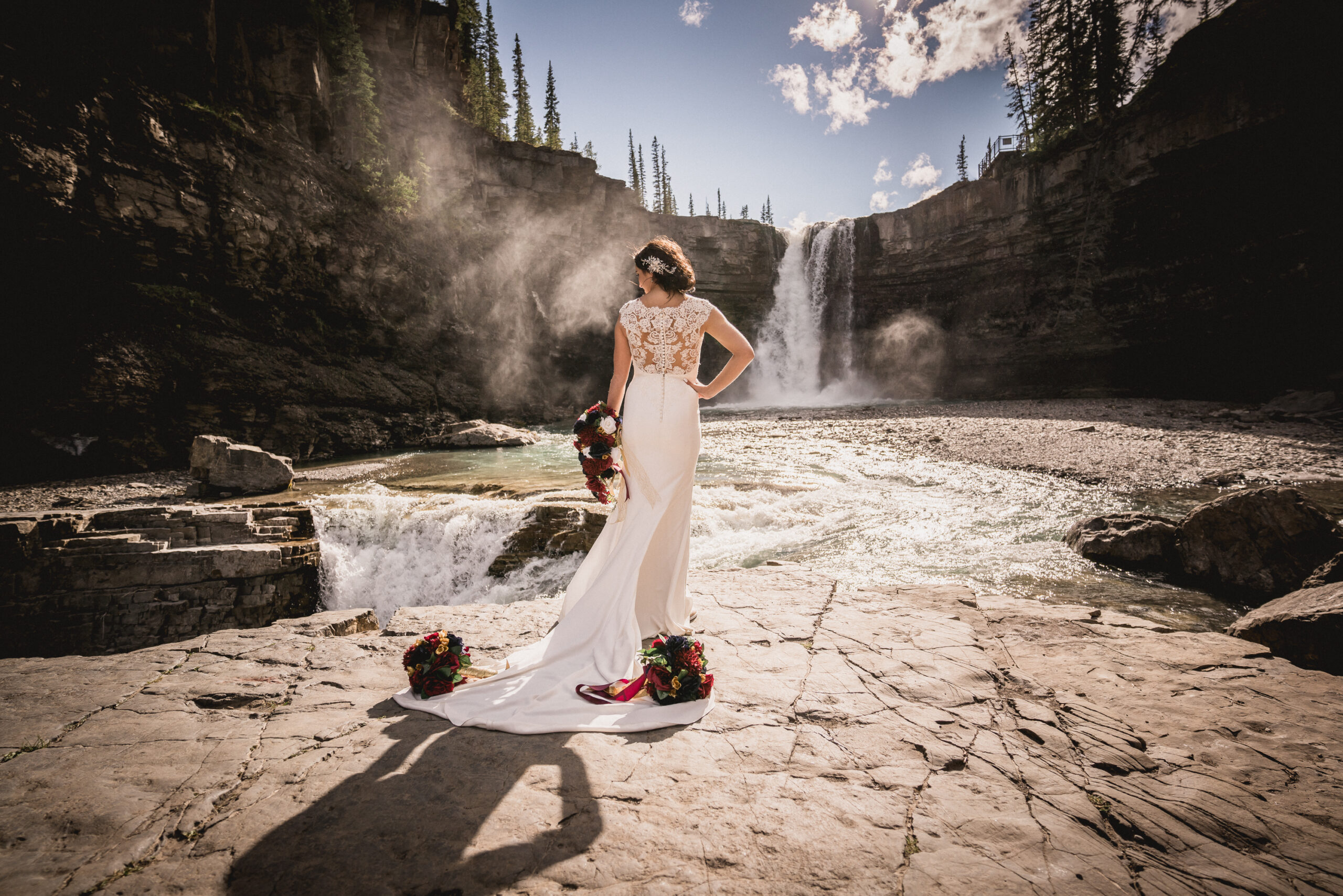 Bride with classic gown with long train, looking over her should in front of waterfall