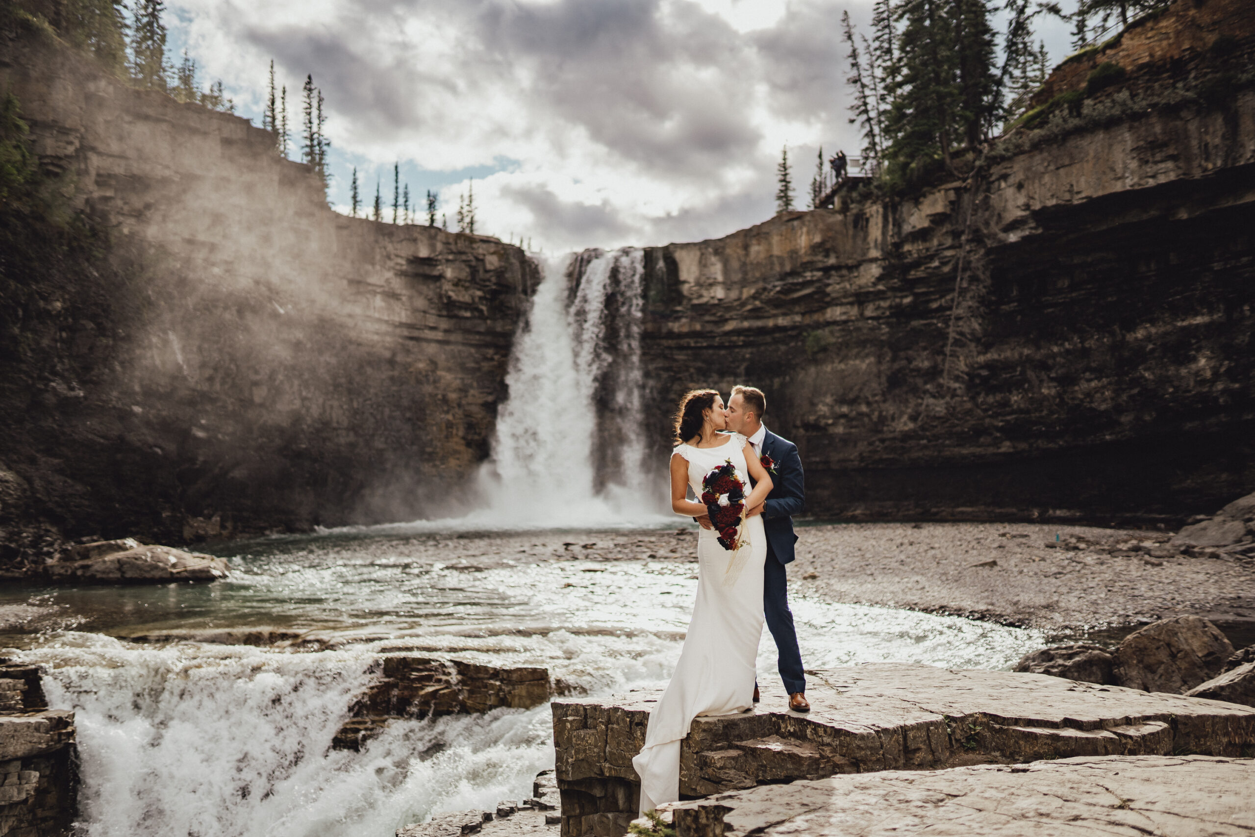 Classic wedding couple kissing in front of waterfall