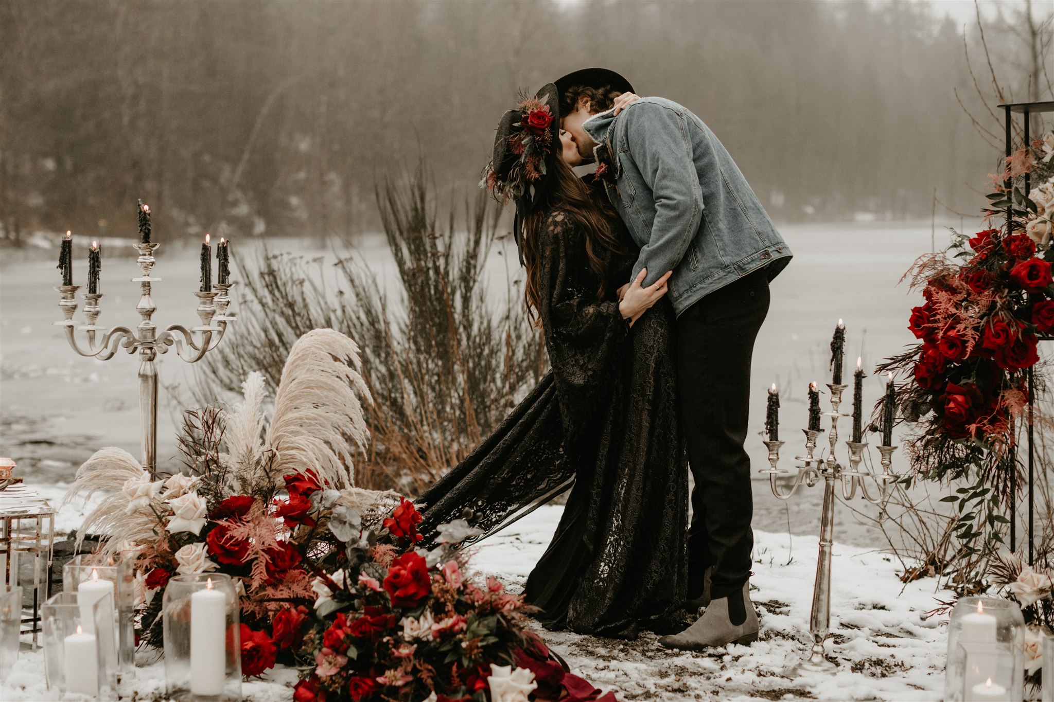Boho bride in black wedding dress kissing boho groom in jean jacket