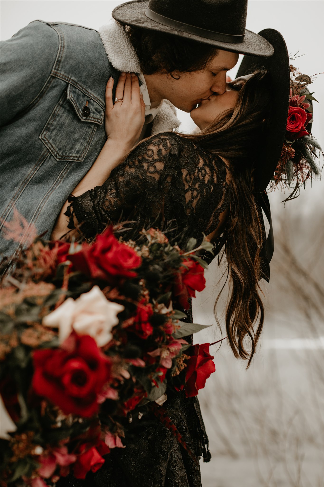 Boho bride in black wedding dress with red wedding bouquet being dipped and kissed by groom