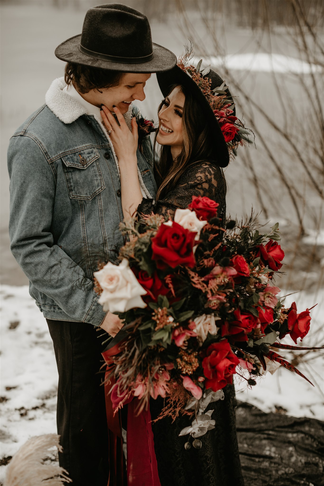 Boho bride with giant red wedding bouquet and black wedding hat with groom in jean jacket