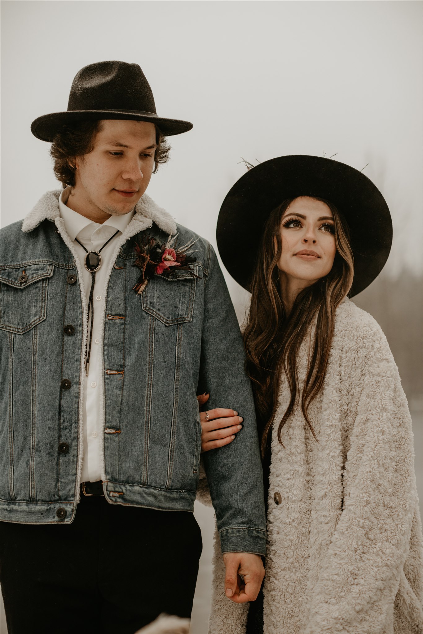 Boho chic bride in furry jacket and groom in jean jacket on snowy river bank