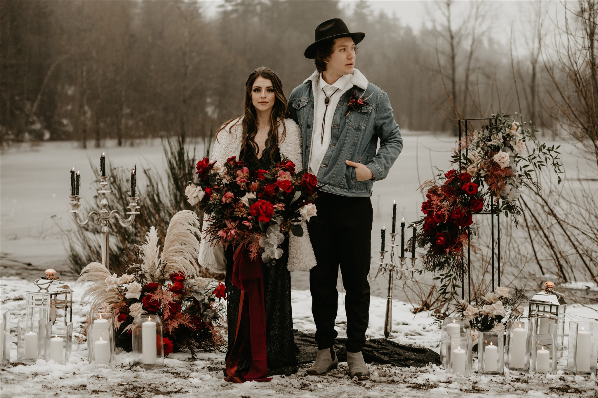Boho chic bride in furry jacket and groom in jean jacket on snowy river bank in front of ceremony set up