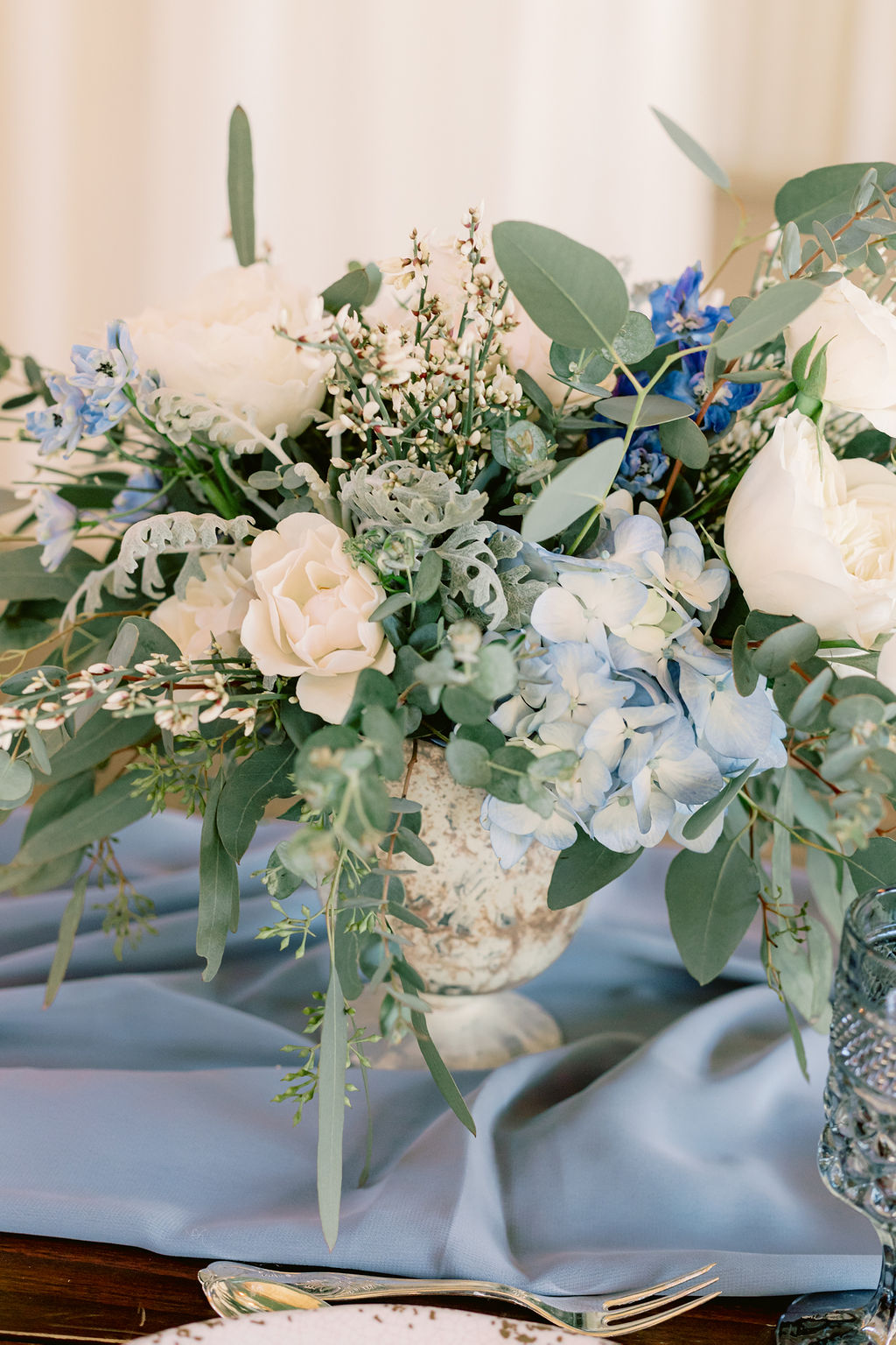 White and light blue wedding flowers center piece on a draped light blue table runner