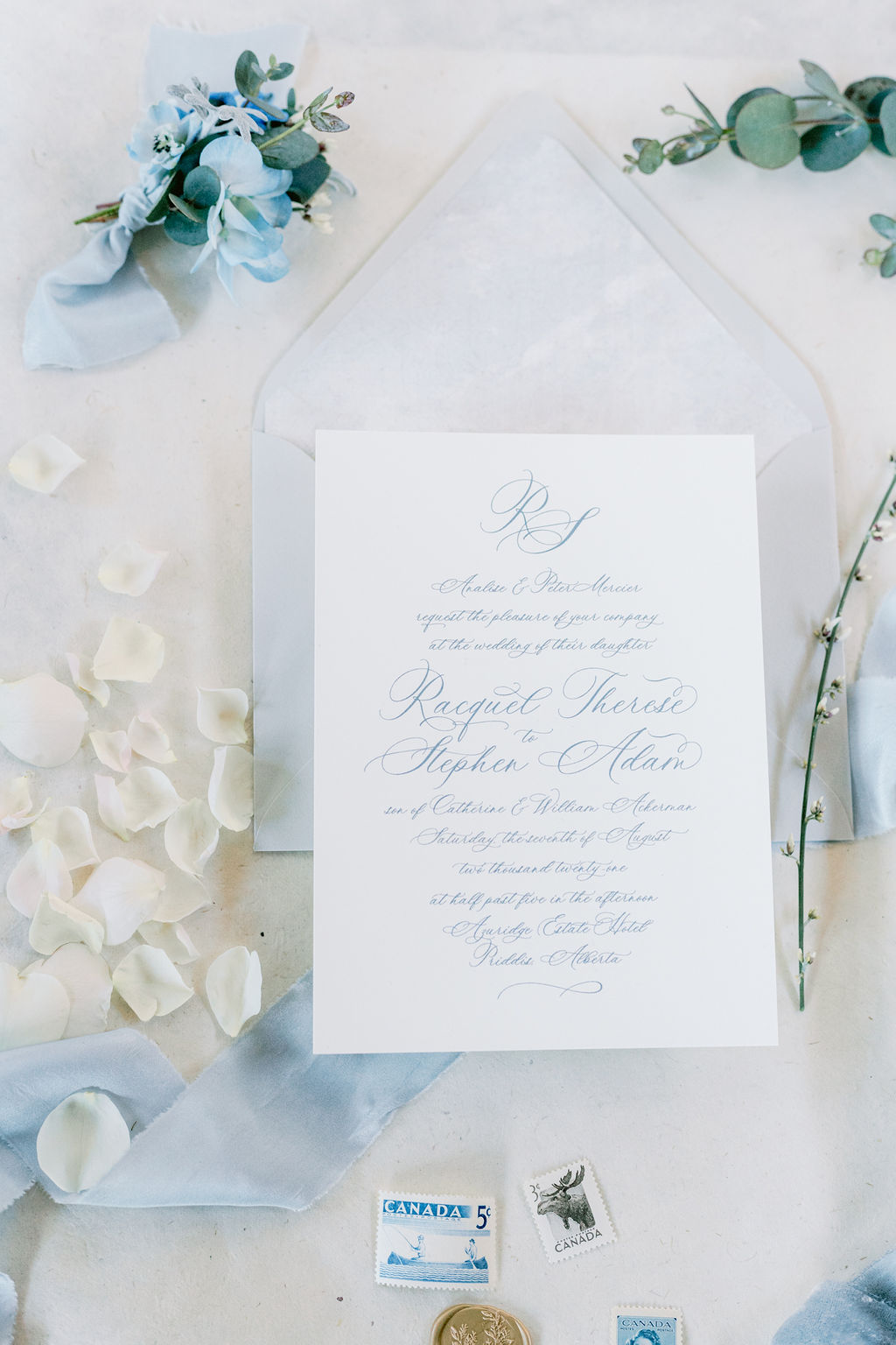 Classic white, ivory and light blue wedding stationery with blue calligraphy and blue flowers against a linen backdrop