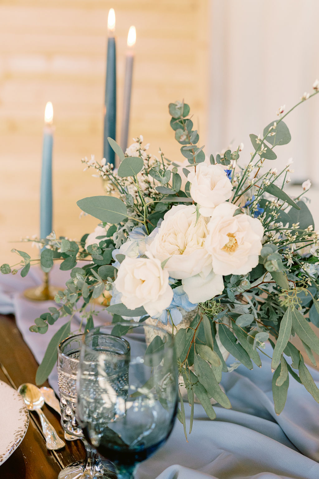 White and light blue wedding flowers center piece with blue candles on blue draped table runner