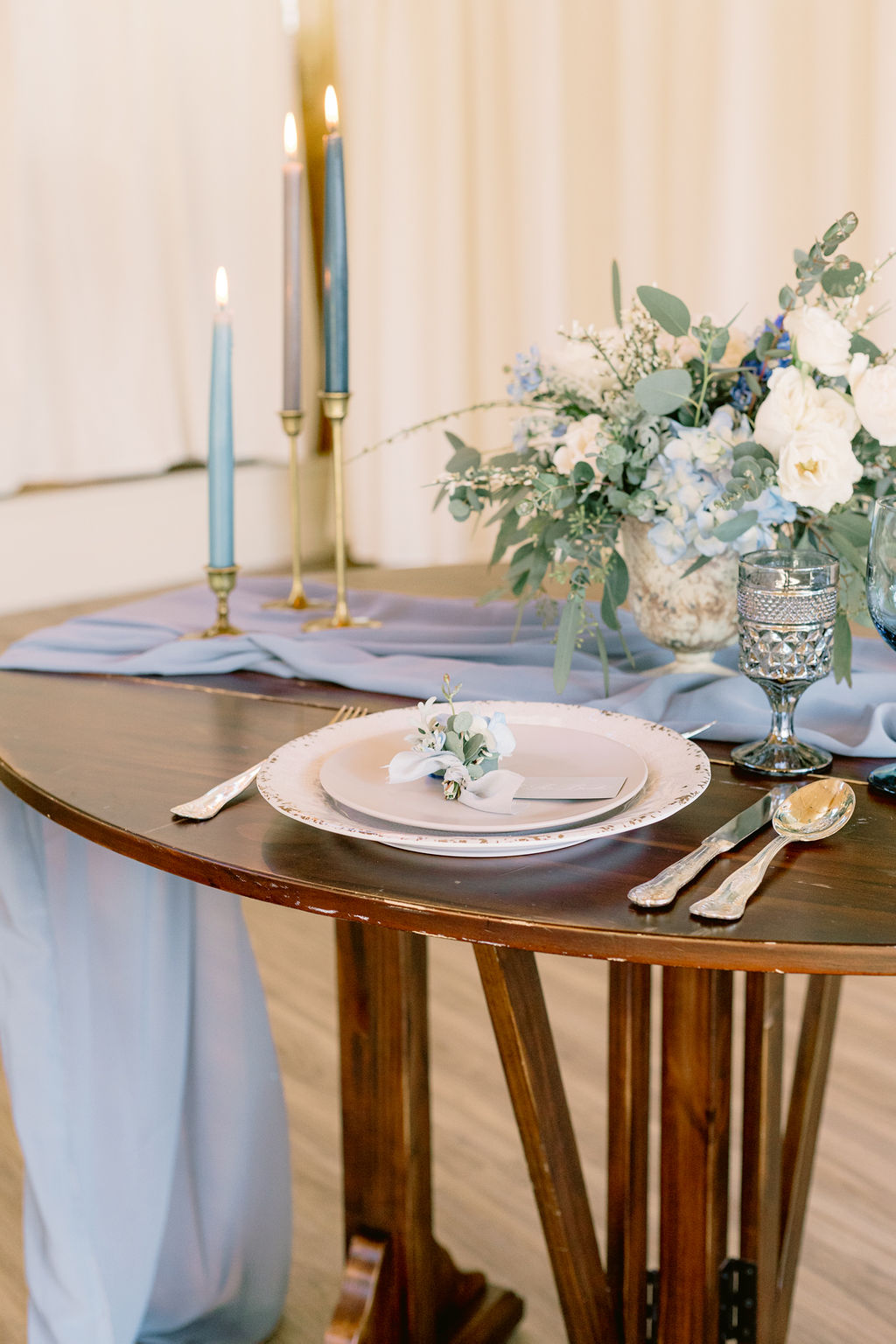 White and light blue wedding flowers center piece with blue candles on blue draped table runner