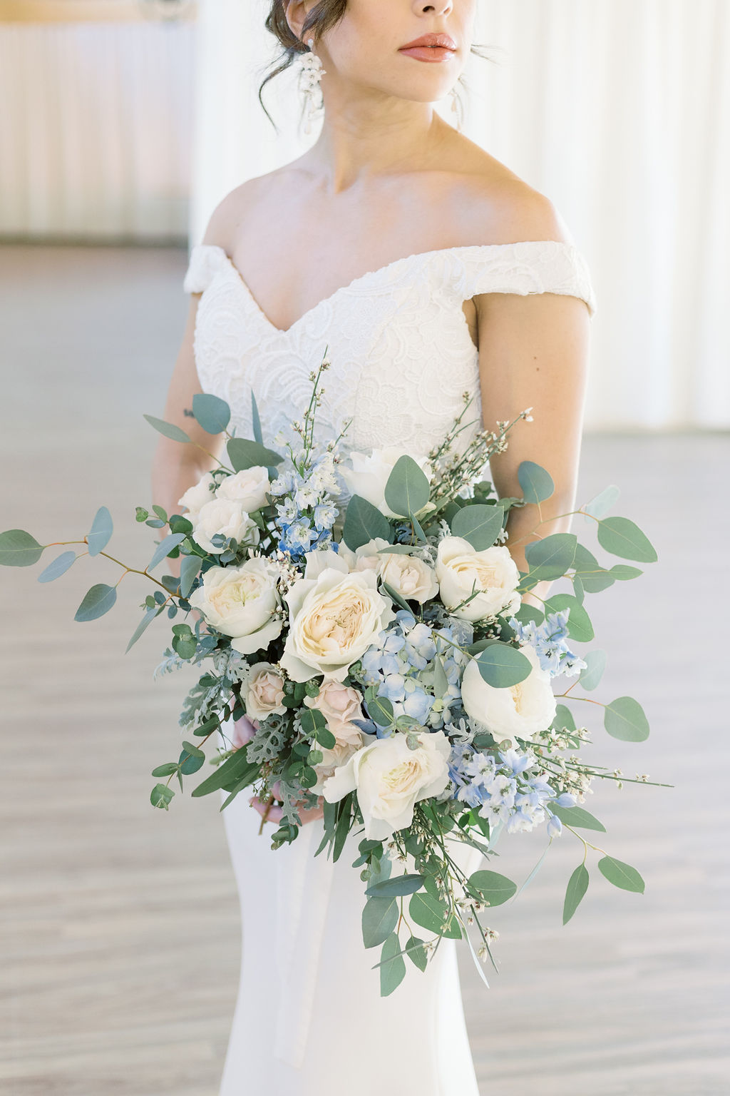 Clasic bride in off the shoulder gown holding white and light blue wedding bouquet
