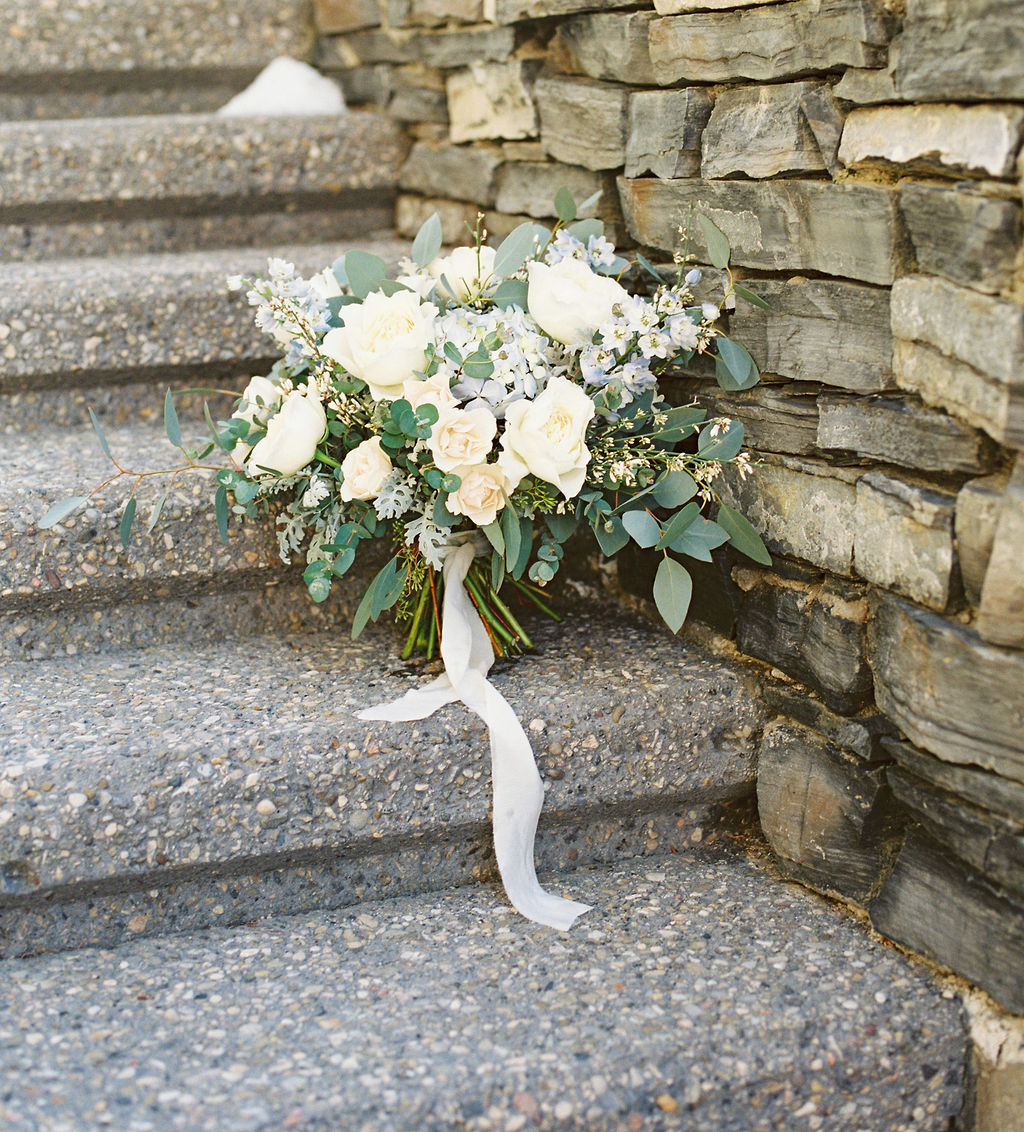 White and blue wedding bouquet with long white ribbon against stone wall