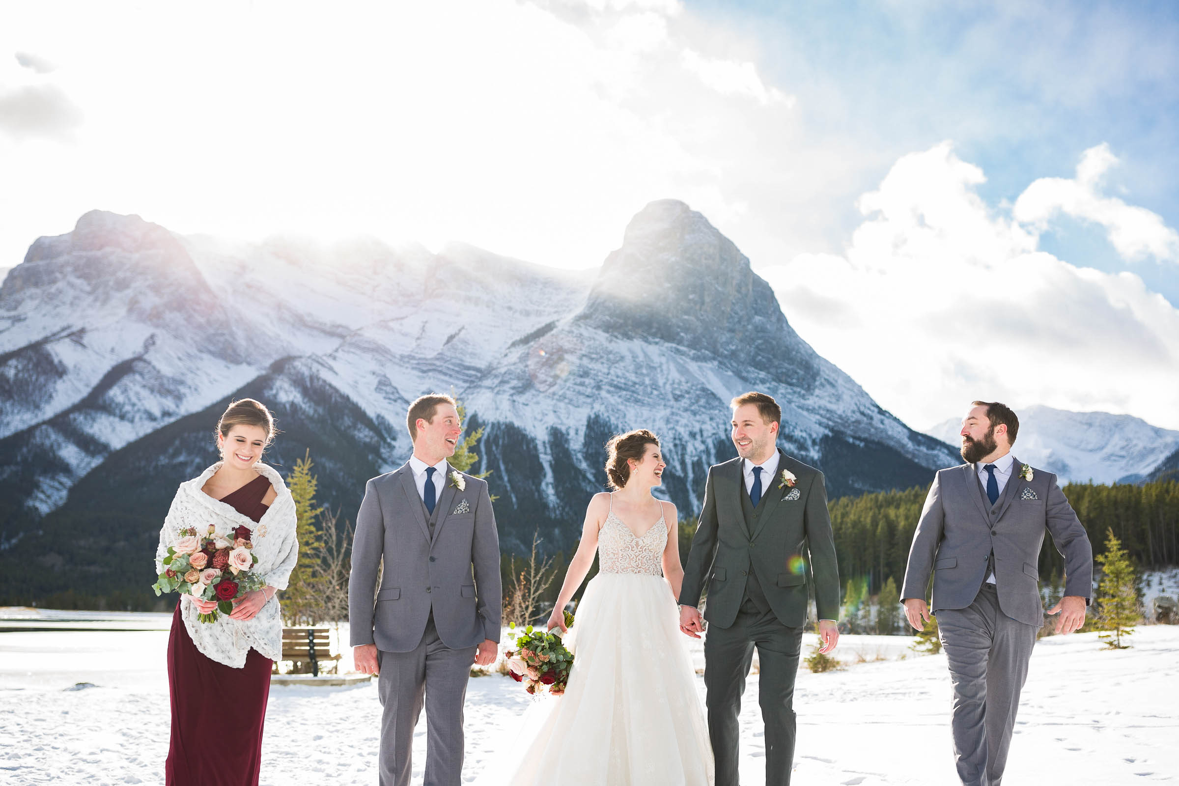 Happy wedding party walking in snow bank with Rocky Mountains in the back