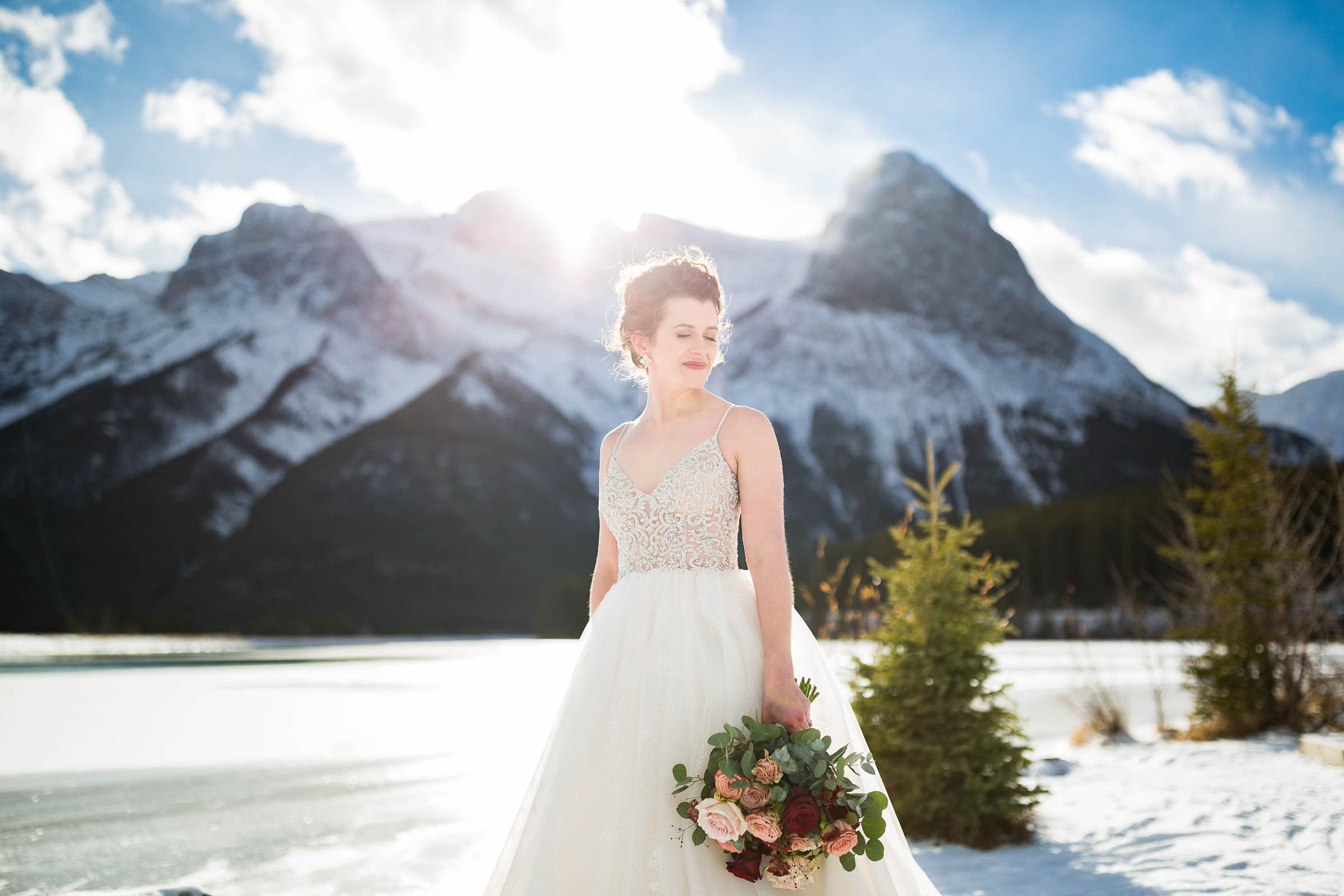 Bride in princess style wedding gown, holding bouquet at her side, in front of mountain backdrop