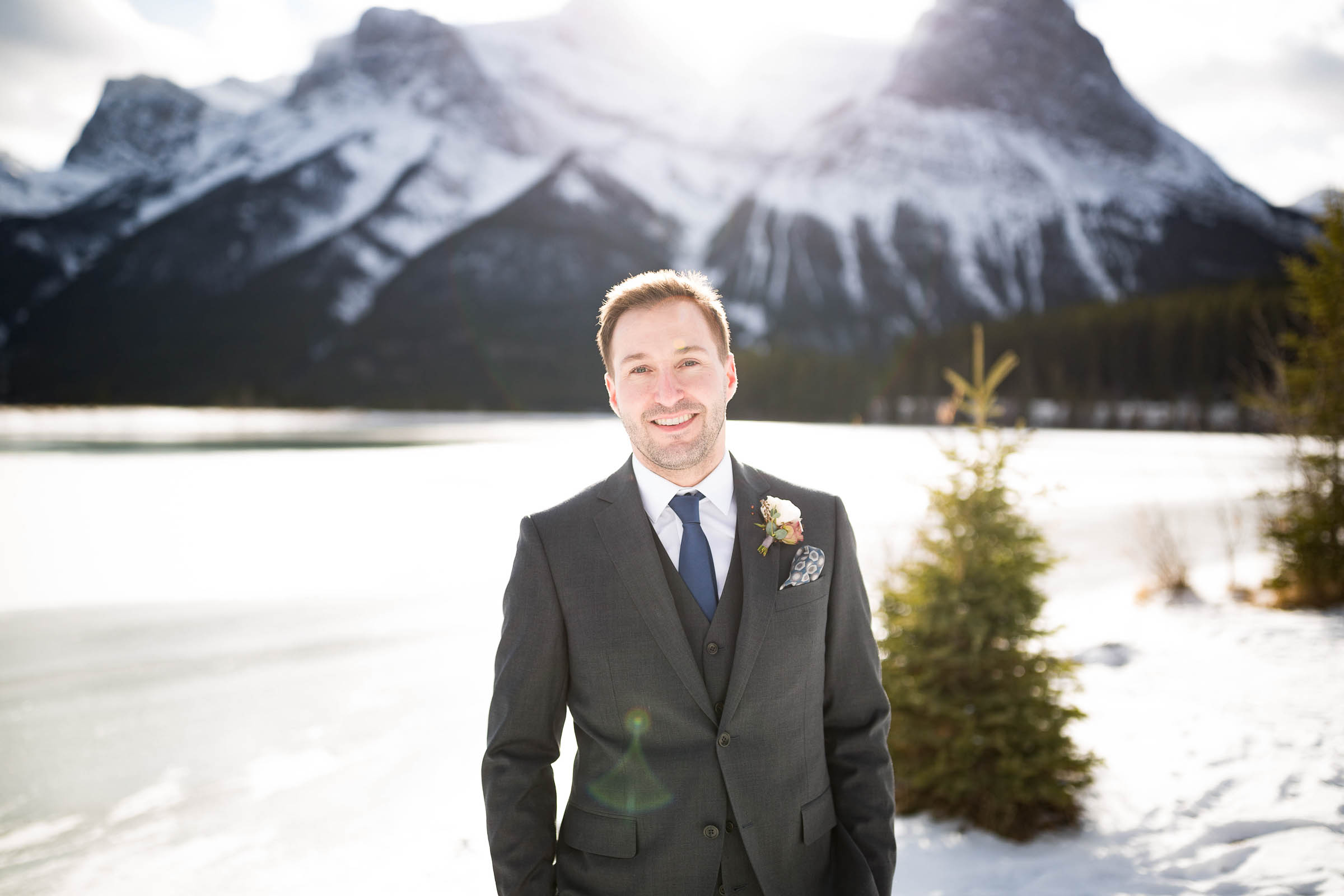 Groom wearing dark grey suit with cobalt blue tie infront of snow mountain backdrop