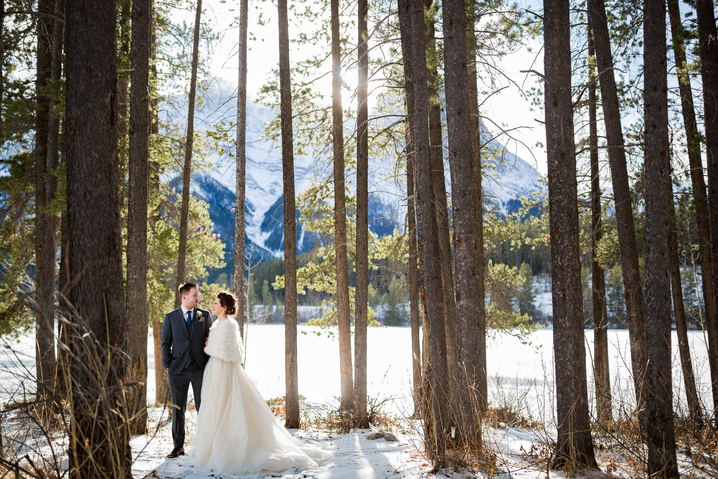 Winter bride in furry jacket and groom walking through woods