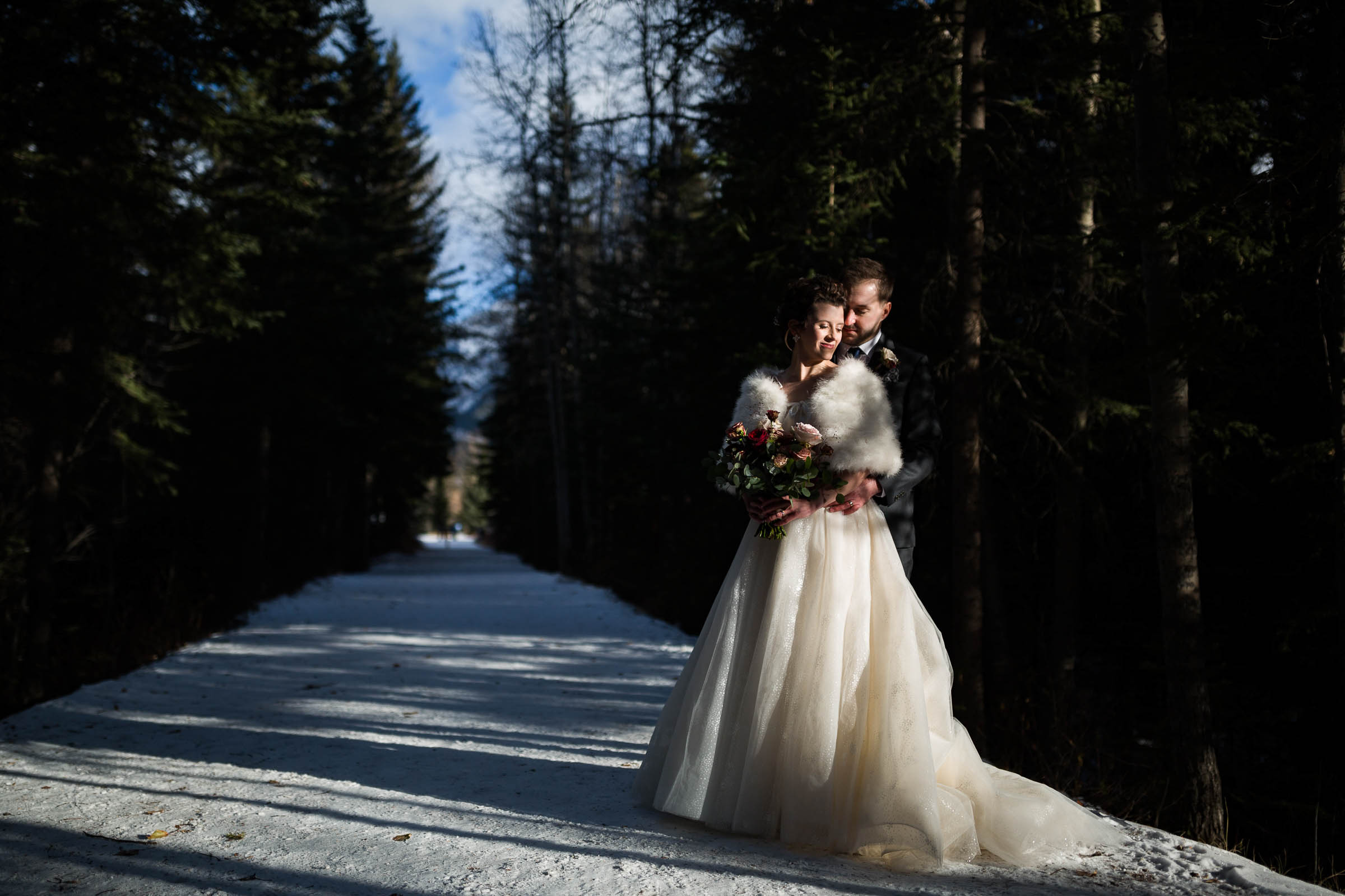 Bride in furry winter wedding jacket with grooms arms wrapped around her