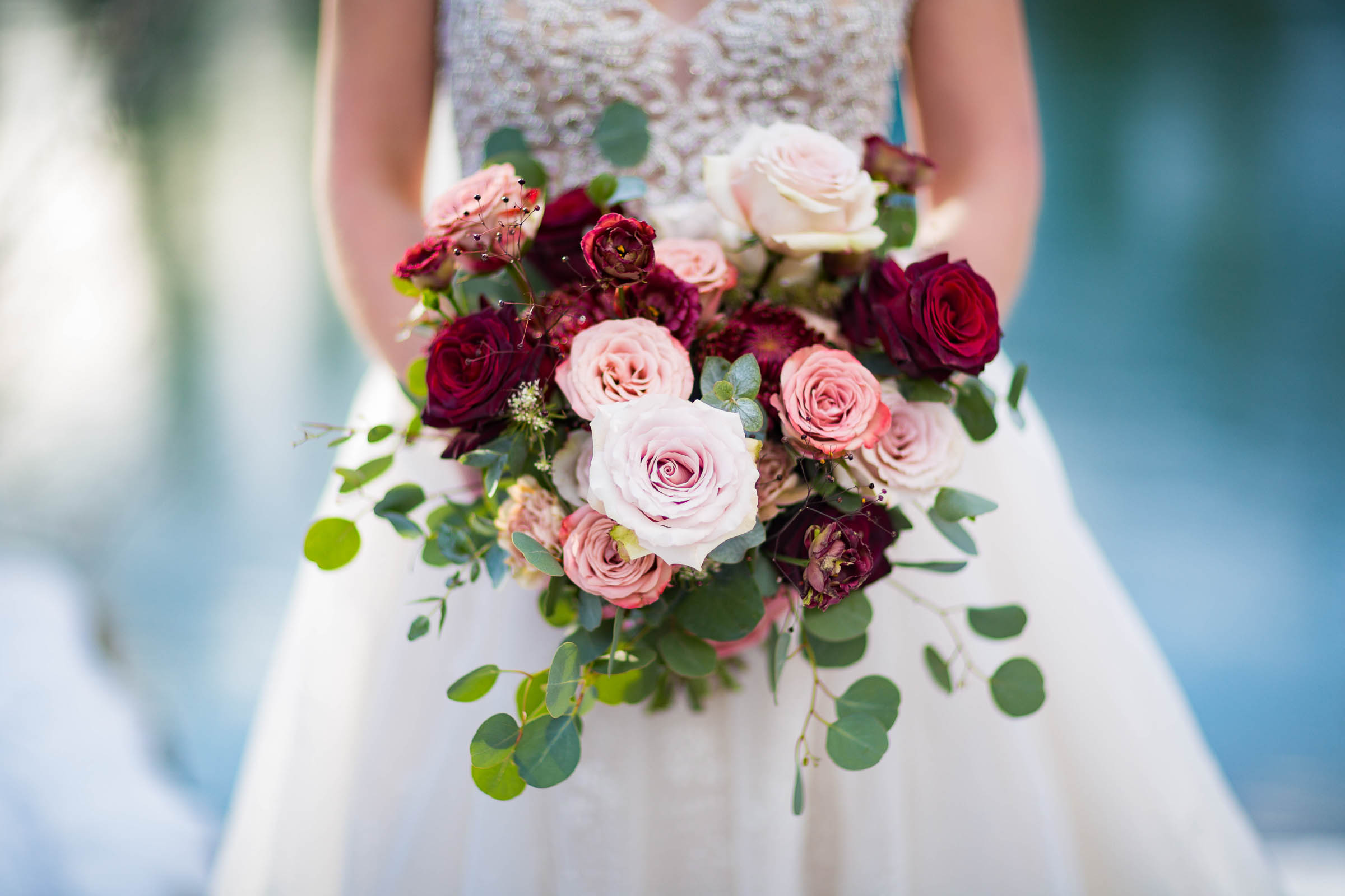 Bride holding wedding bouquet of red roses, blush roses and white roses with greenery