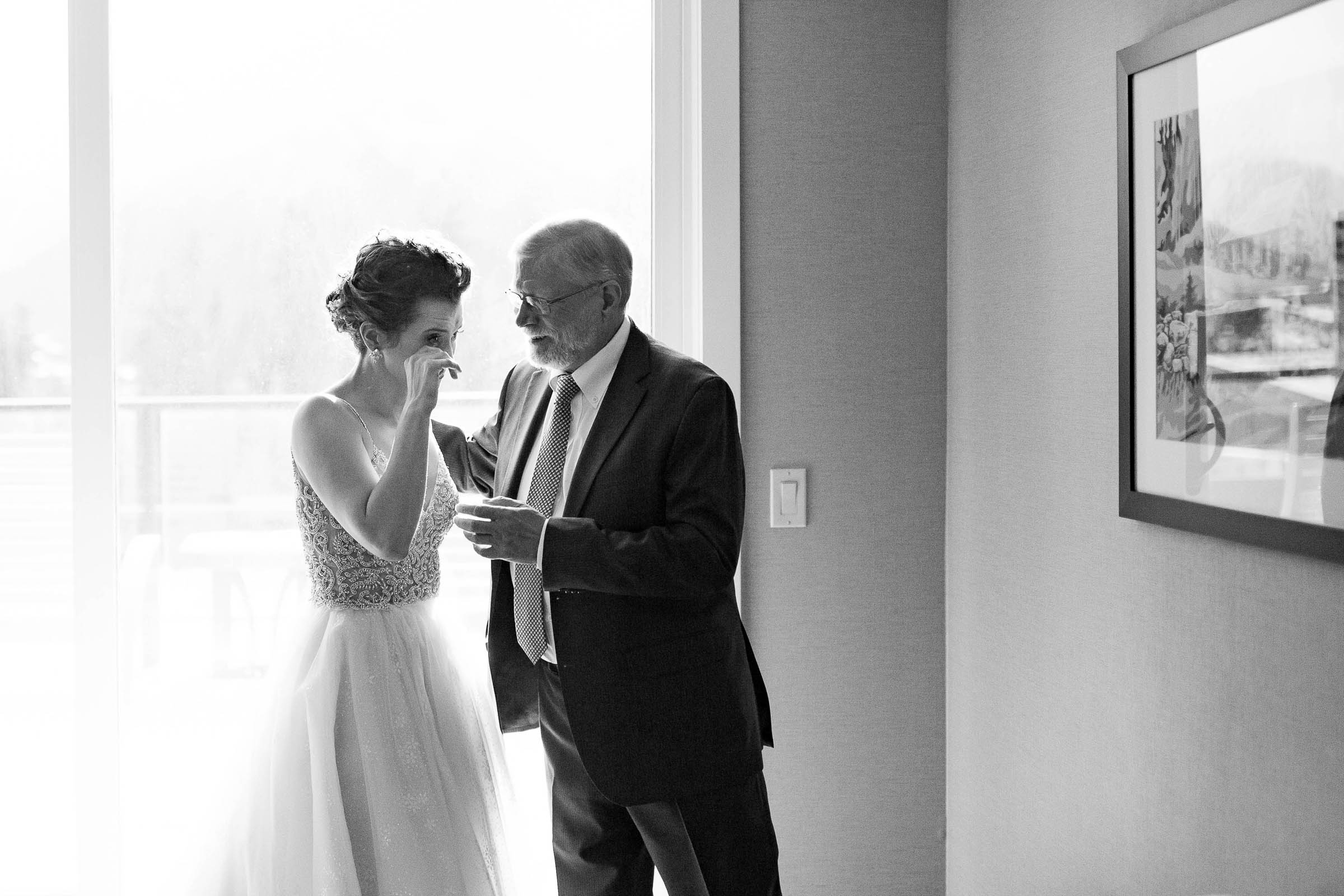 Bride wiping a tear from her eye as her father speaks to her before her wedding
