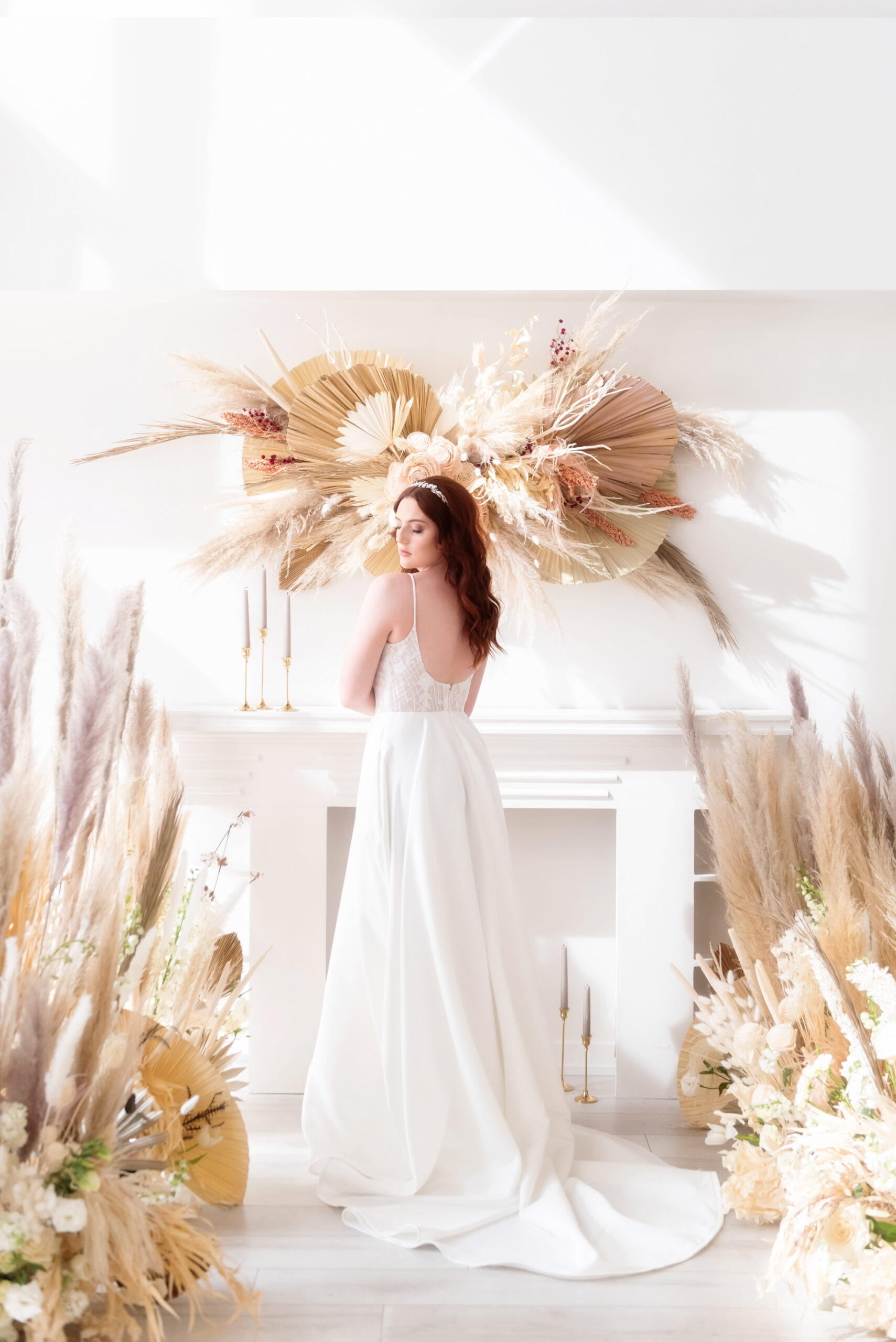 Bride with red hair in white wedding dress surrounded by natural boho wedding decor in white wedding venue