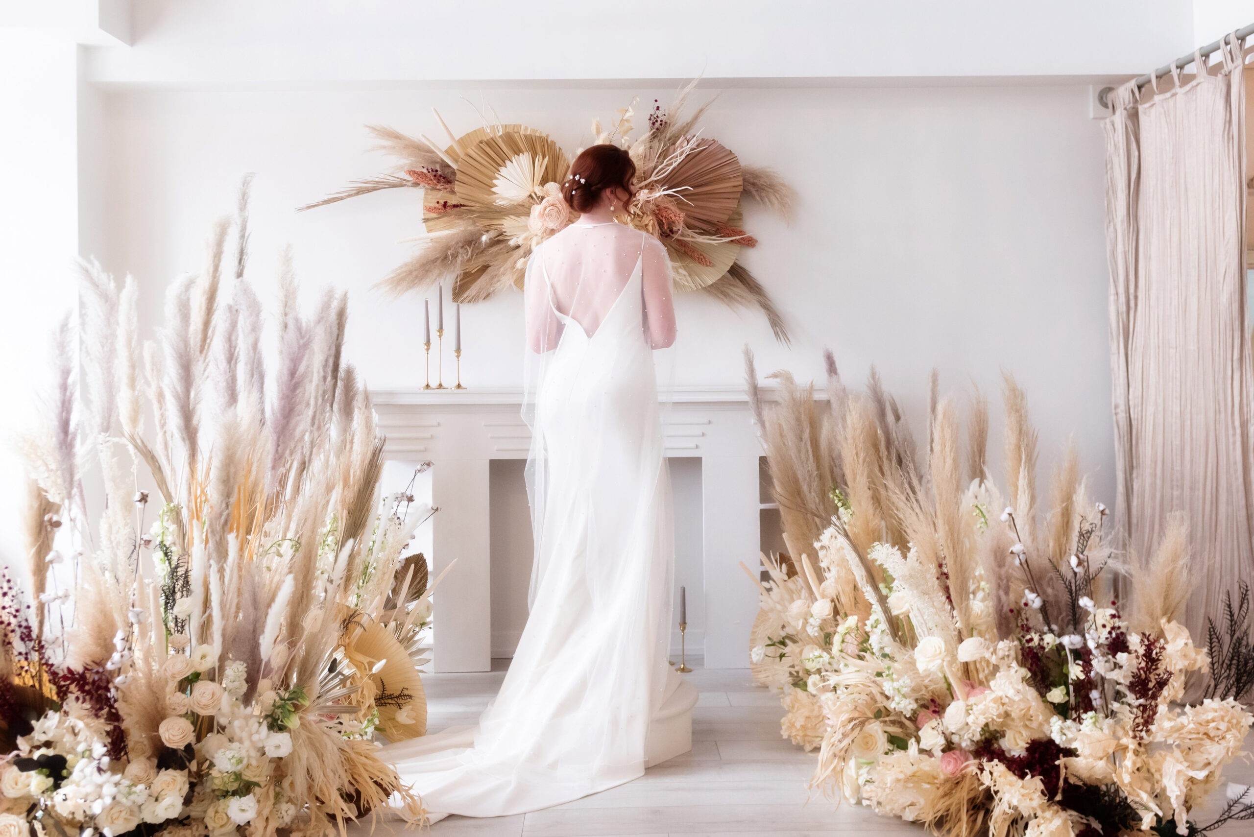 Back of bride in a modern wedding gown in front of cream and ivory boho wedding decor