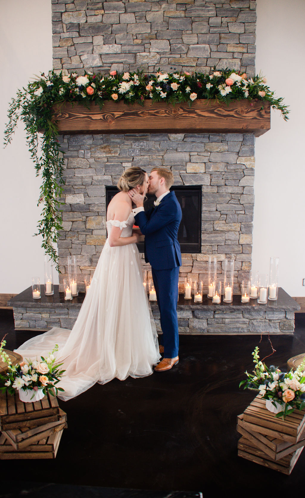 Bride and Groom kissing in front of elegant stone fireplace with candles and flowers