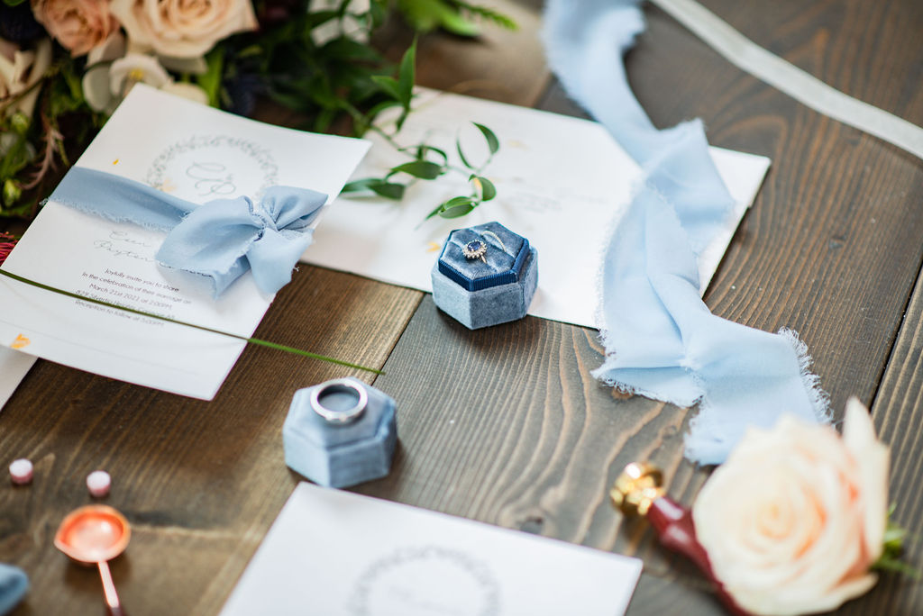 Weddings rings in blue wedding boxes surrounded by blue ribbons and ivory wedding stationery
