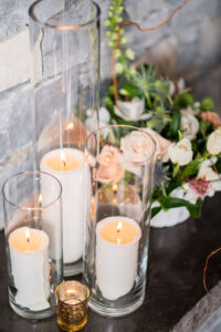 Candles in tall clear vases next to wedding flowers