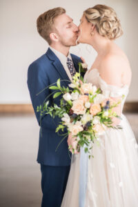 Bride and groom kissing, holding large peach and white wedding bouquet