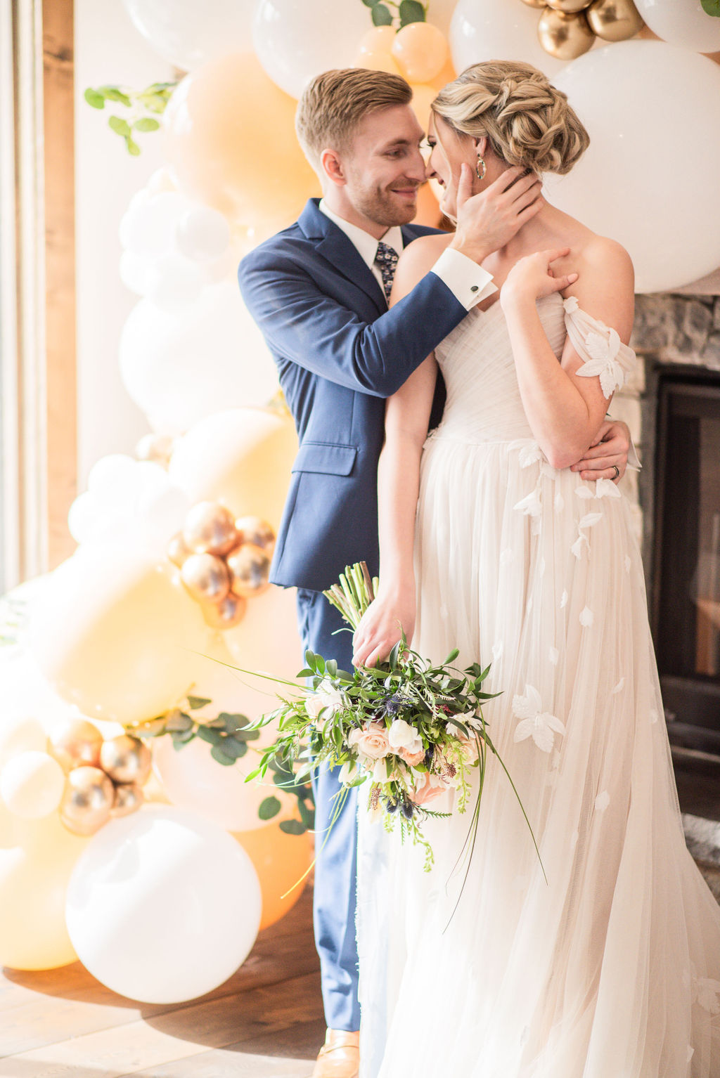Groom in a blue suit, kissing a bride in a cream wedding dress, holding a bouquet of flowers