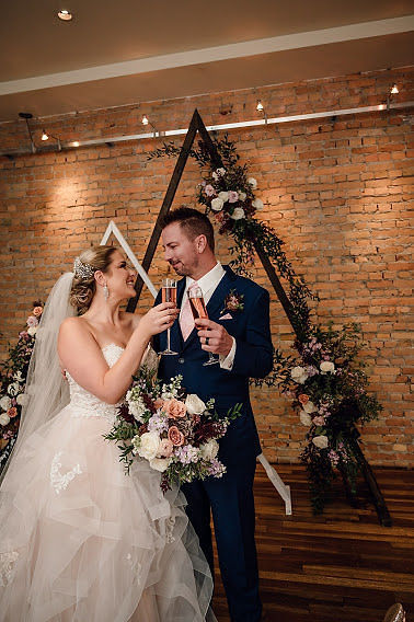 Bride and Groom celebrating infront of geometric wedding ceremony decor bride holding bouquet of blush and burgundy flowers
