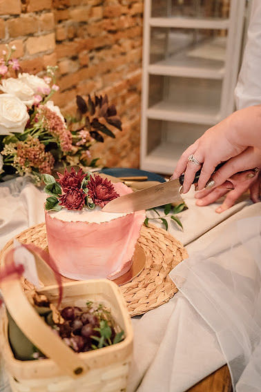 Bride and groom cutting into small blush wedding elopement cake with blush water color details and burgundy flowers