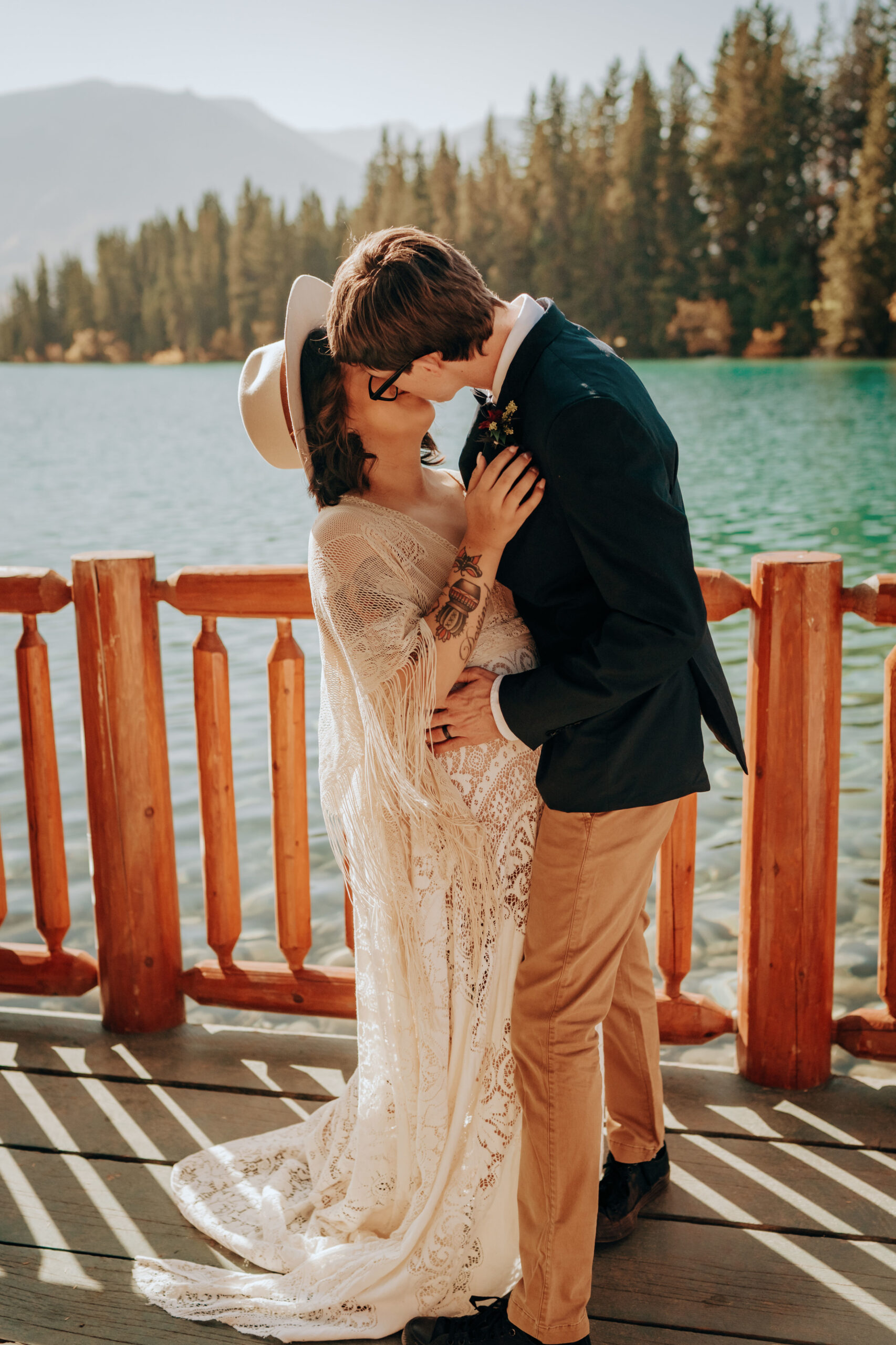 Boho wedding couple kisses I Do on deck overlooking lake in Rocky Mountains