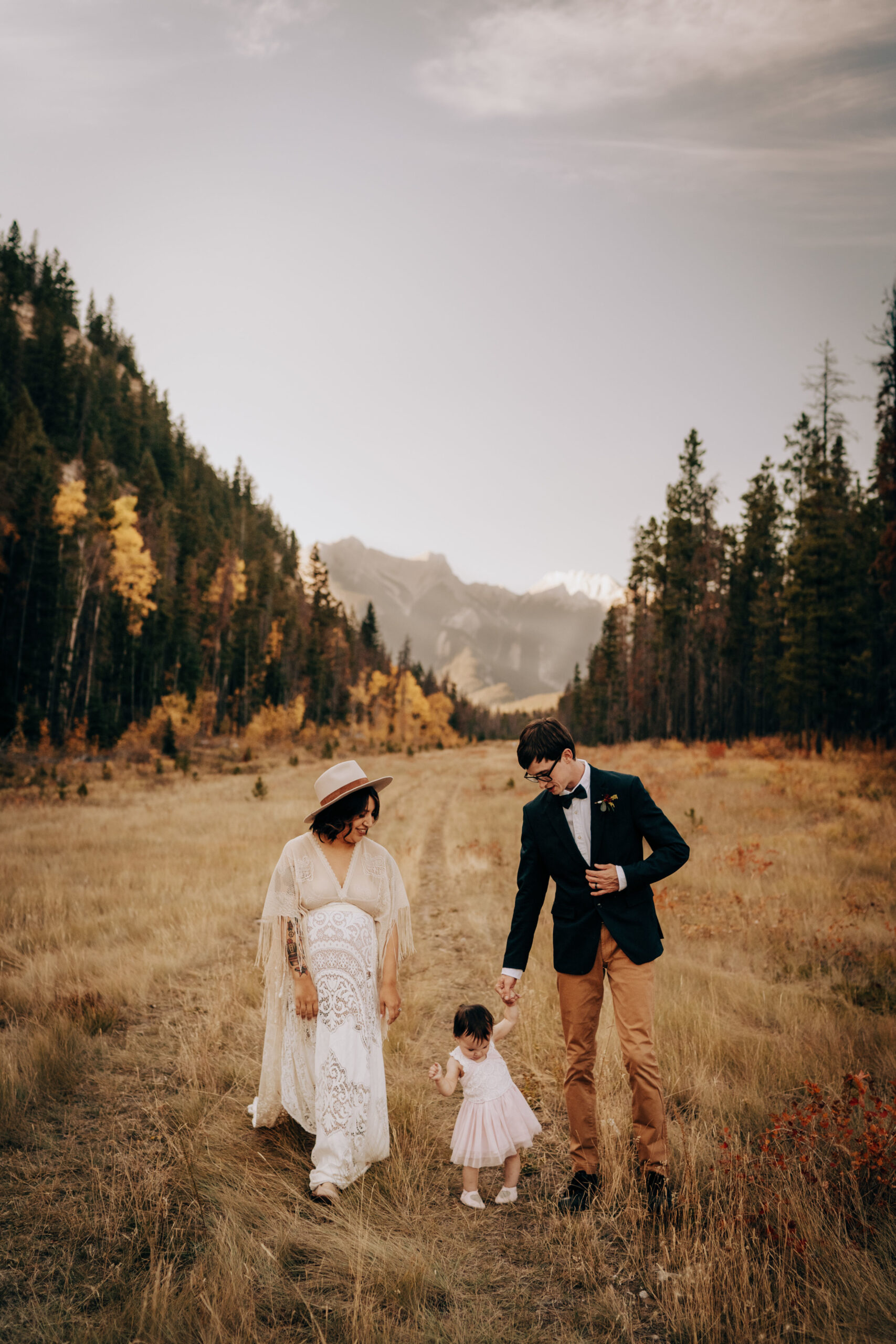 Boho bride and groom walking through valley holding hands with their boho baby