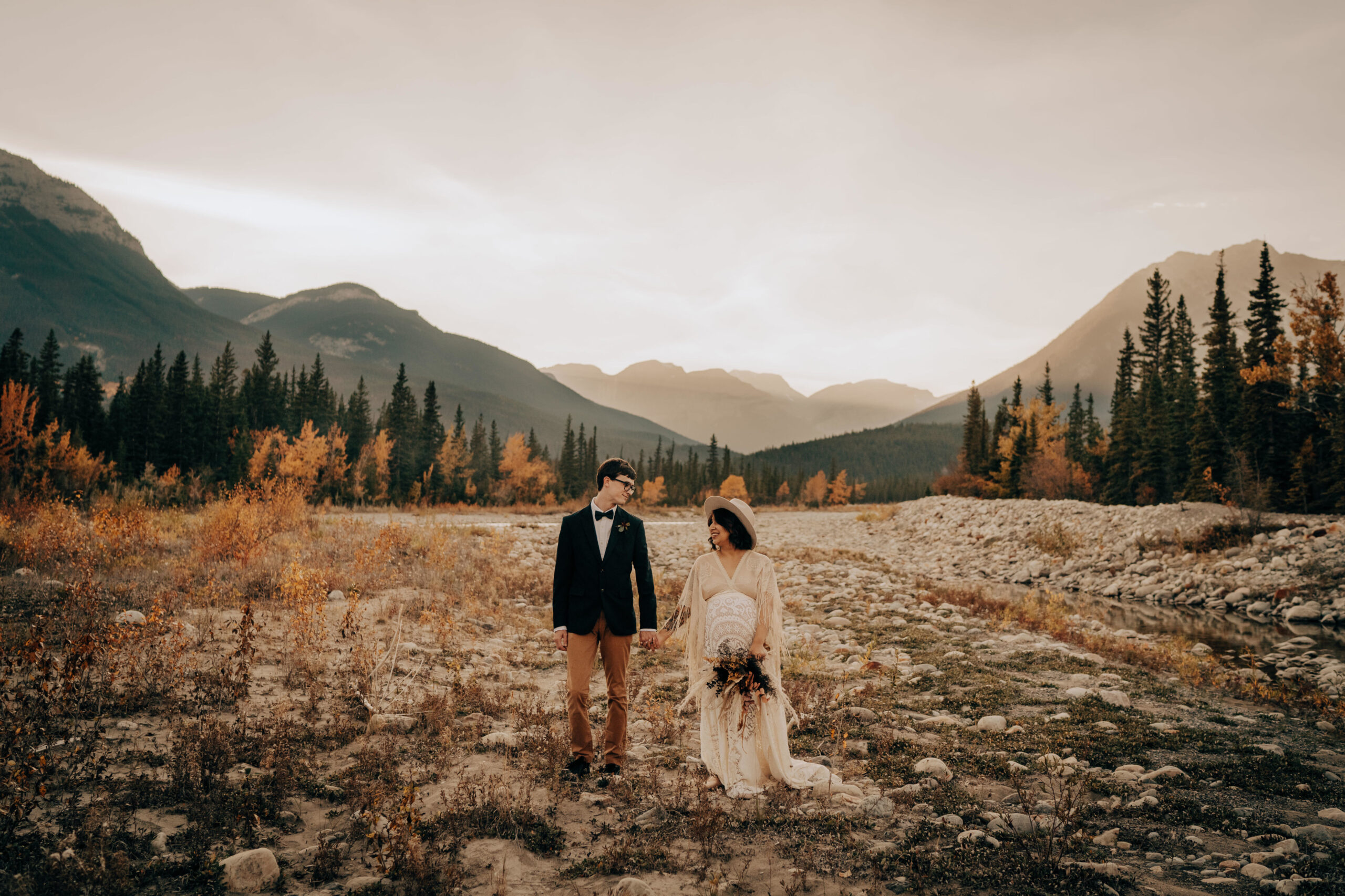 Boho bride and boho groom standing in valley, holding hands and looking at each other