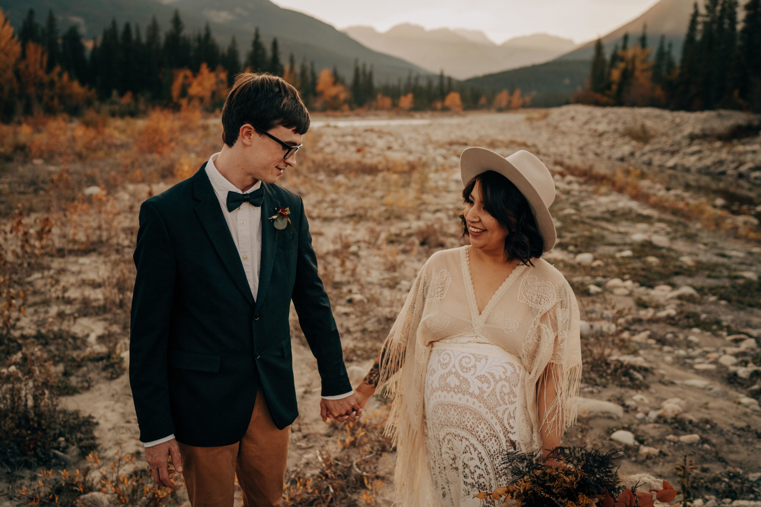 Boho bride and boho groom standing in valley, holding hands and looking at each other