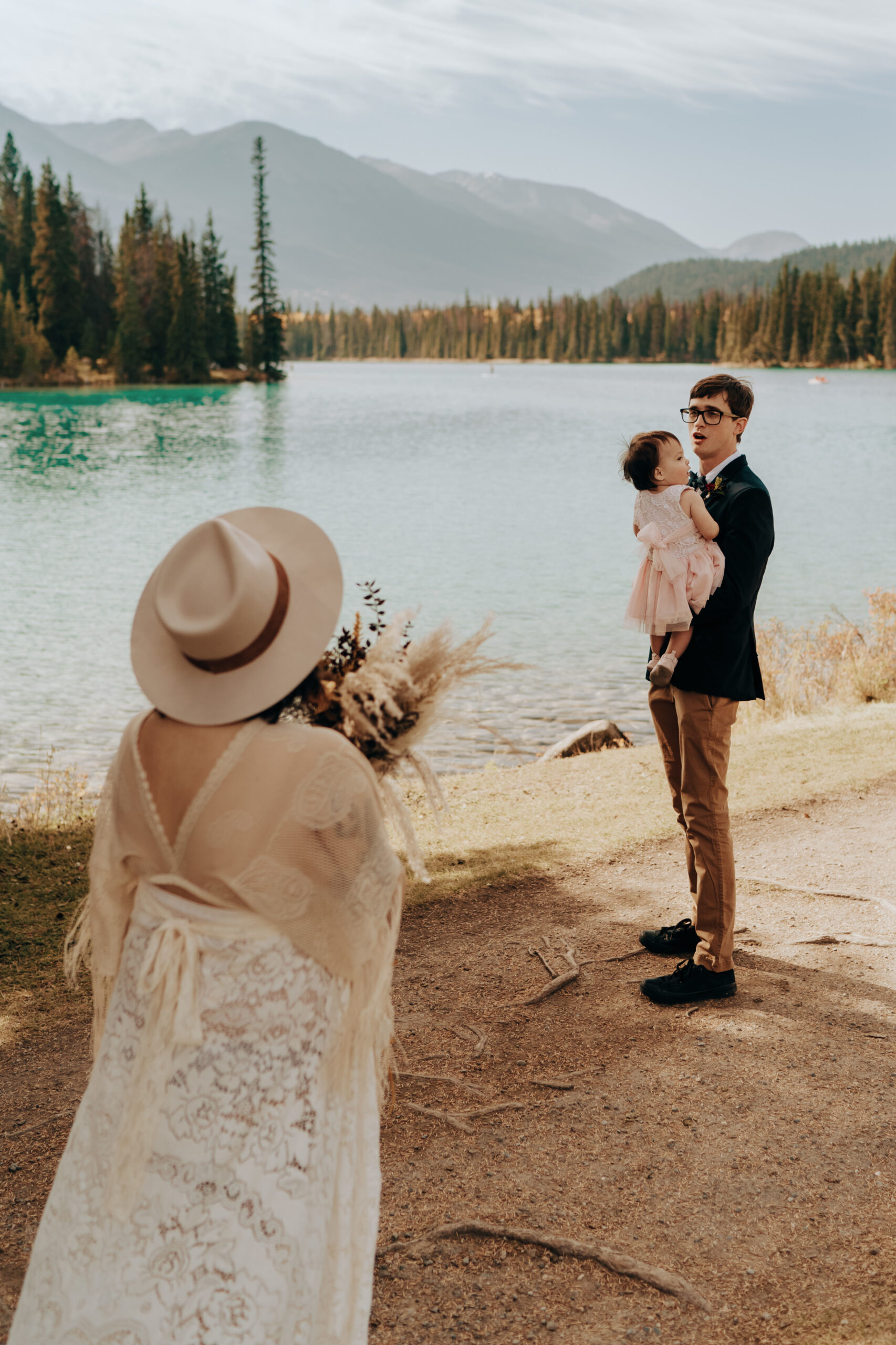 Boho bride in cute hat has first look with boho groom holding adorable baby