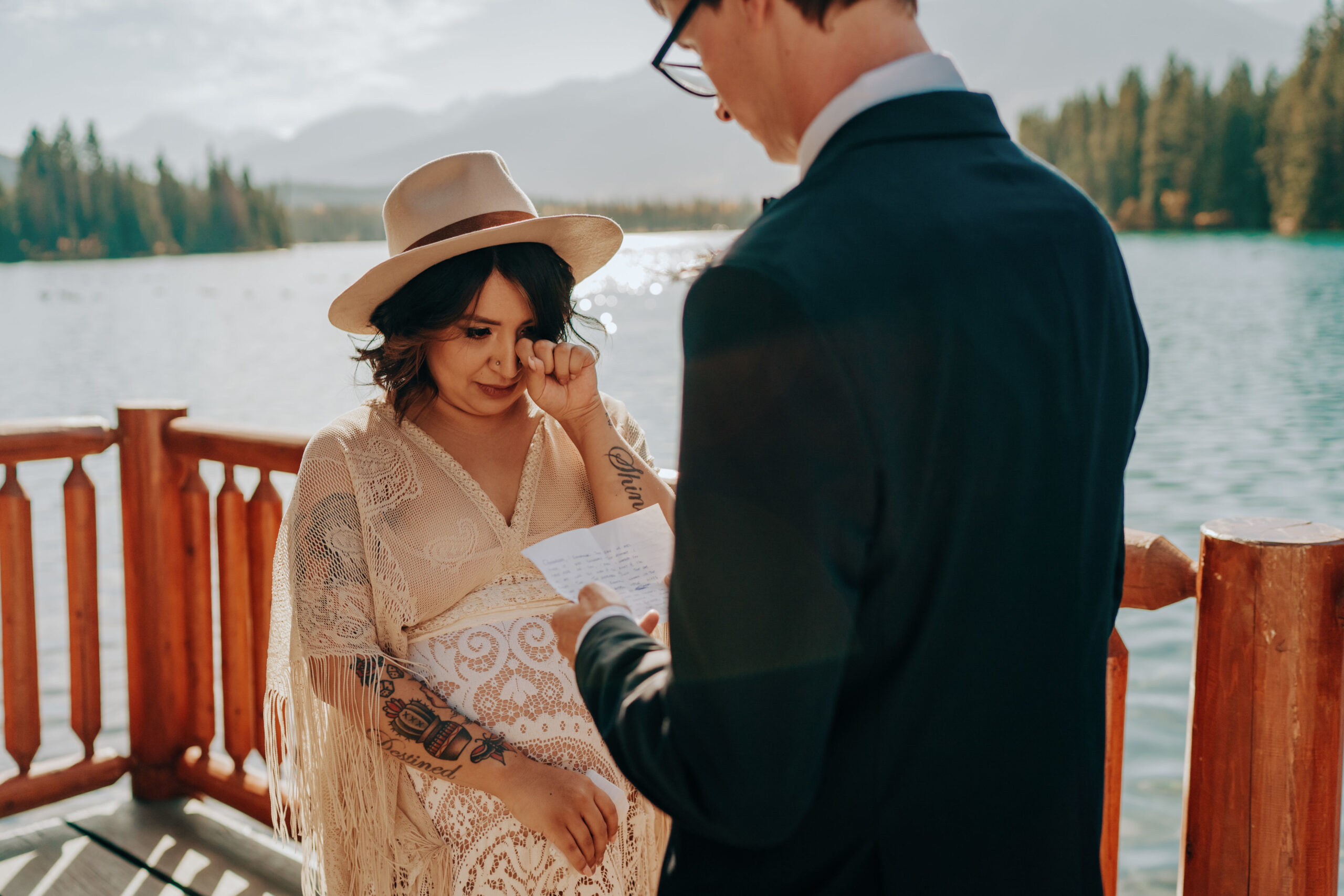 Boho bride in hat saying vows on deck overlooking lake