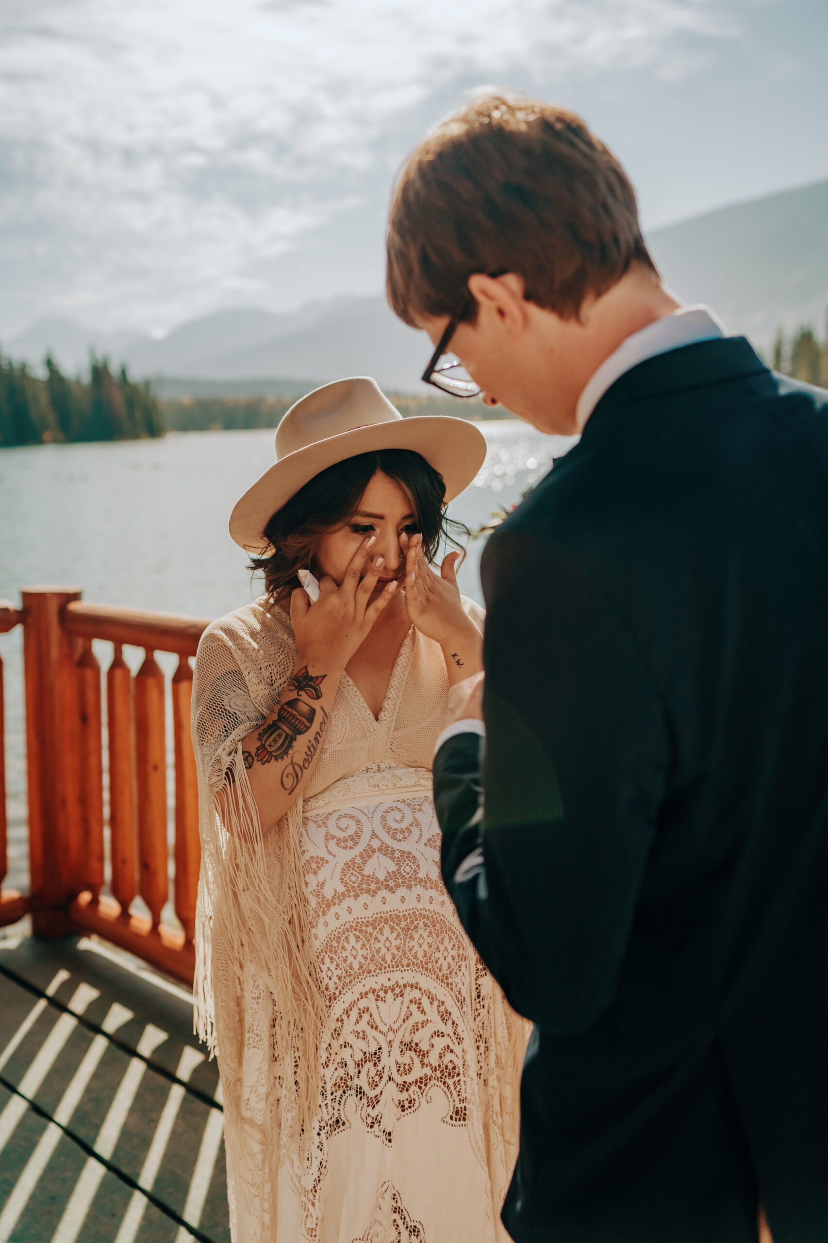 Boho bride in hat saying vows on deck overlooking lake