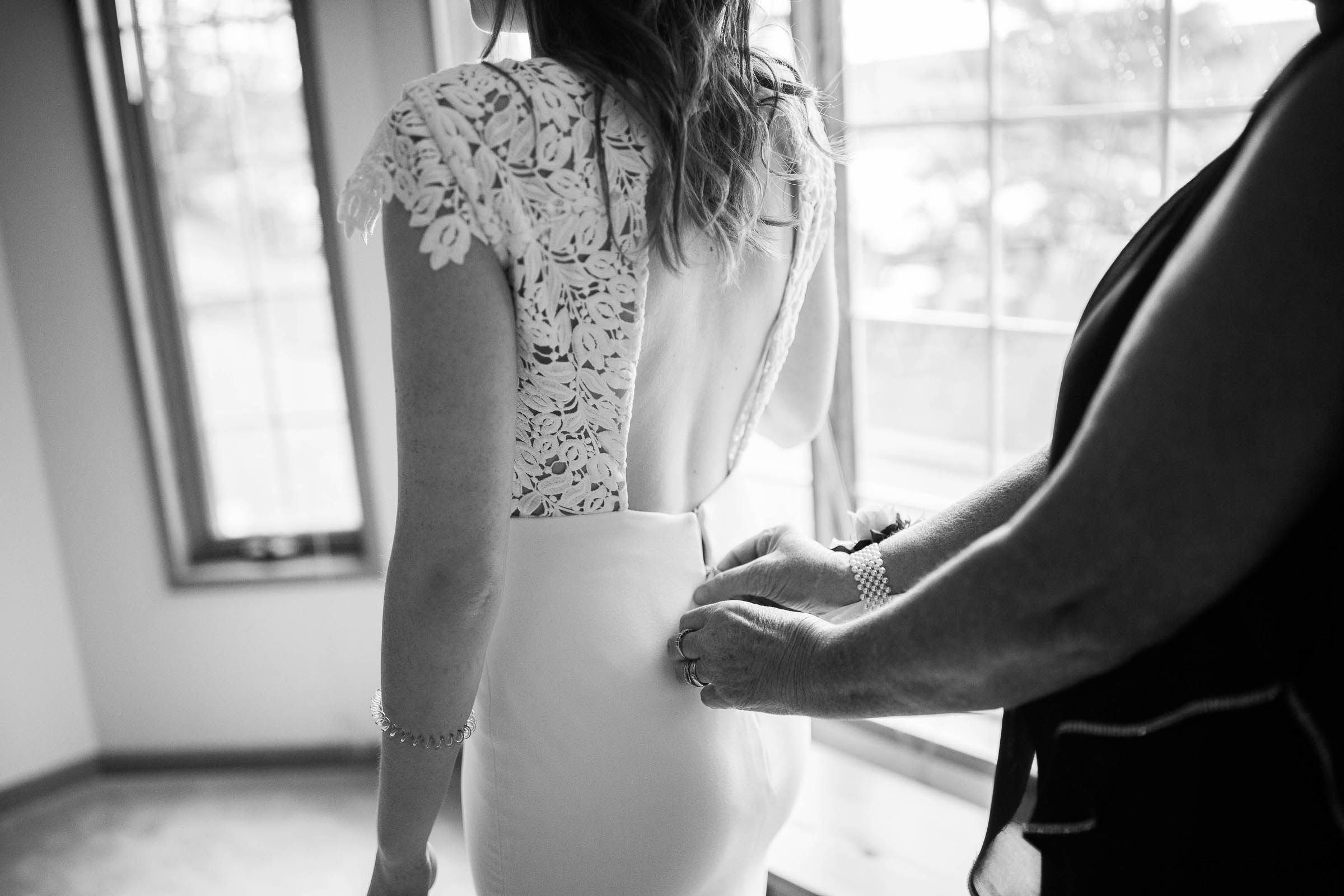 Black and white photo of bride having her lace gown done up