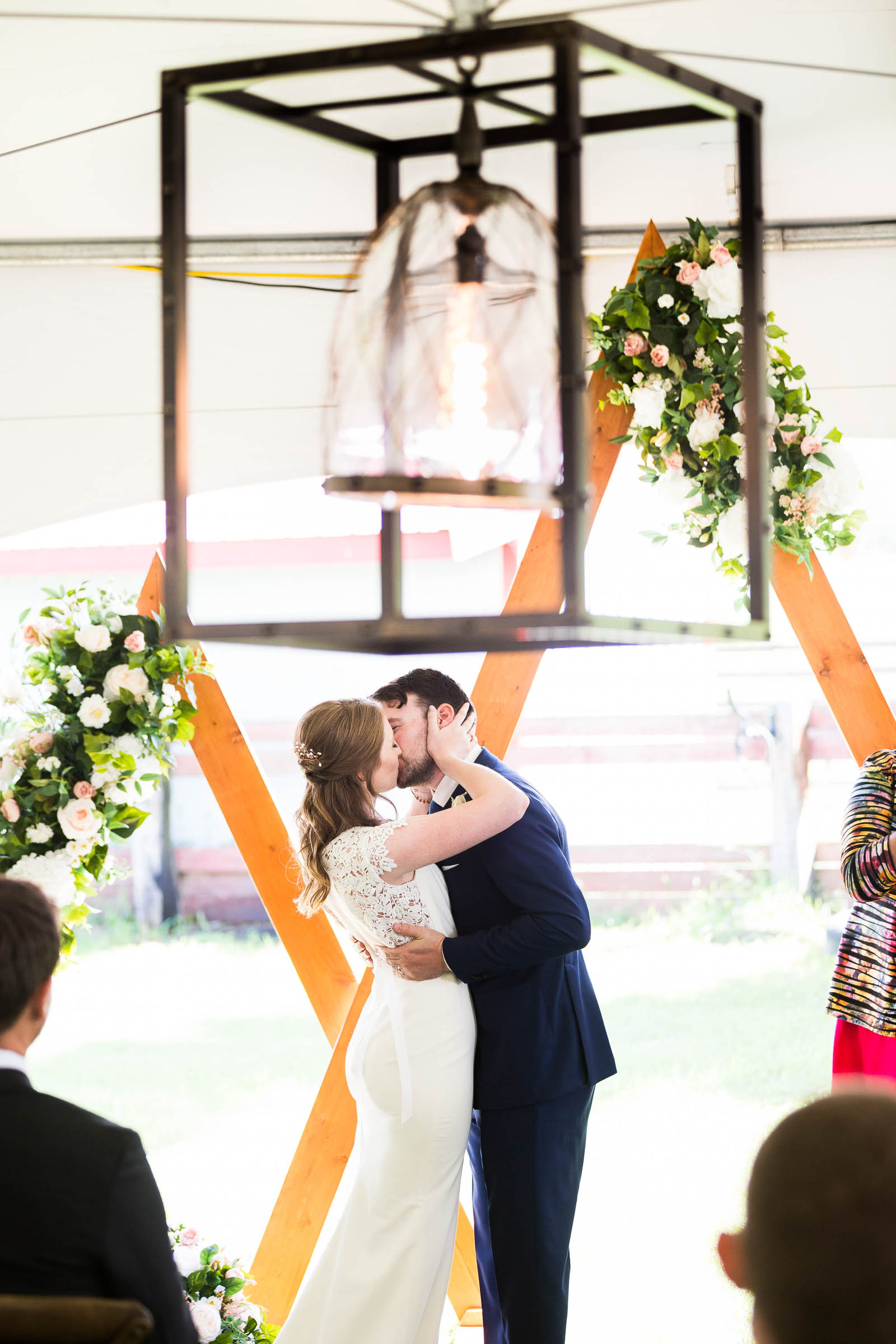 Couple kissing under rustic square chandelier in front of triangle geometric wedding arch
