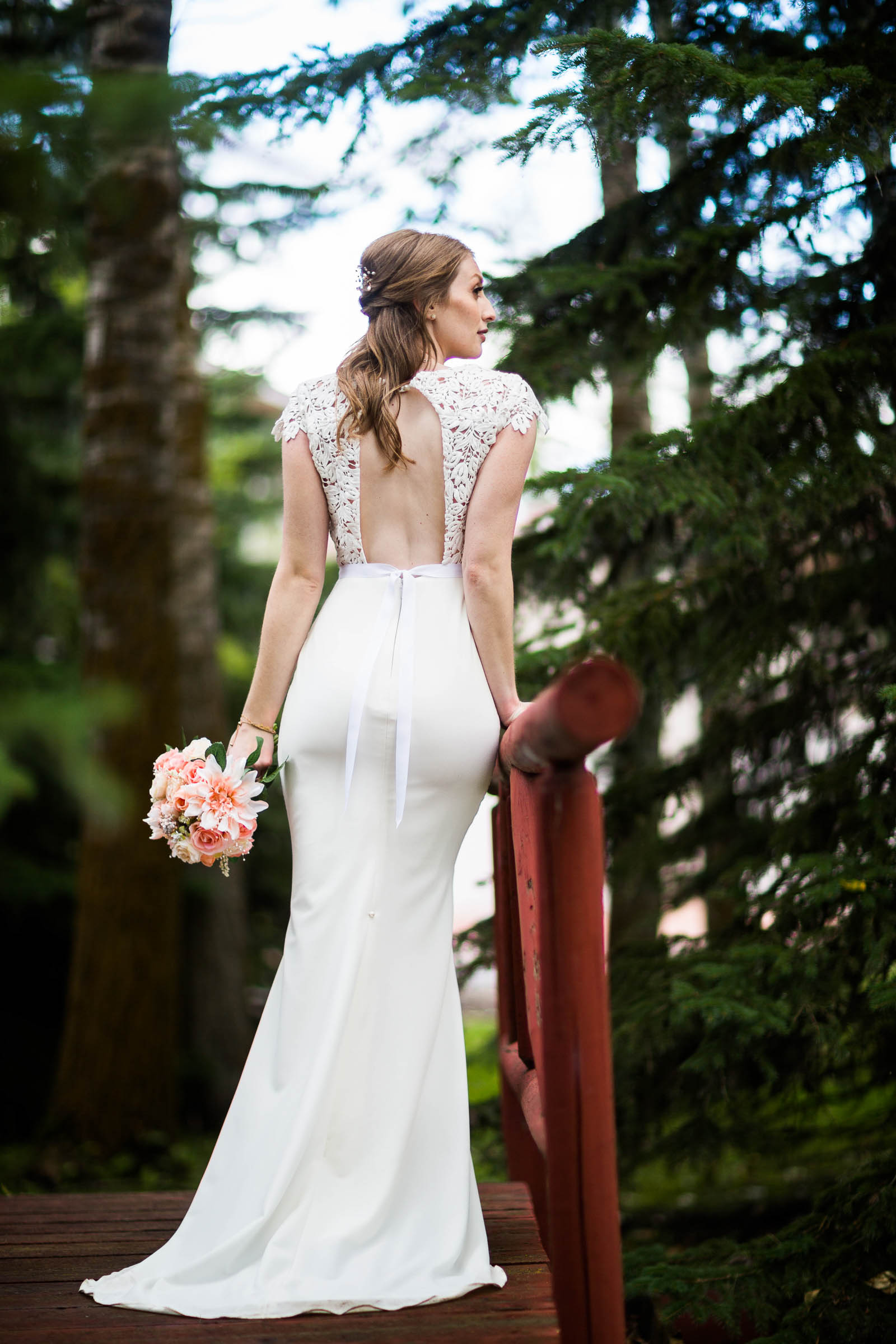 Bride in classic fitted wedding gown with keyhole back, lace bodice and lace cap sleeves holding blush bouquet
