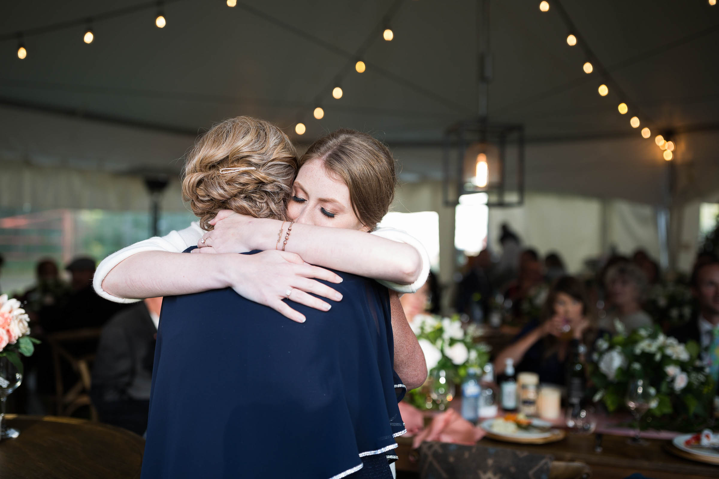 Bride hugging father during father daughter dance in tented wedding under table lights