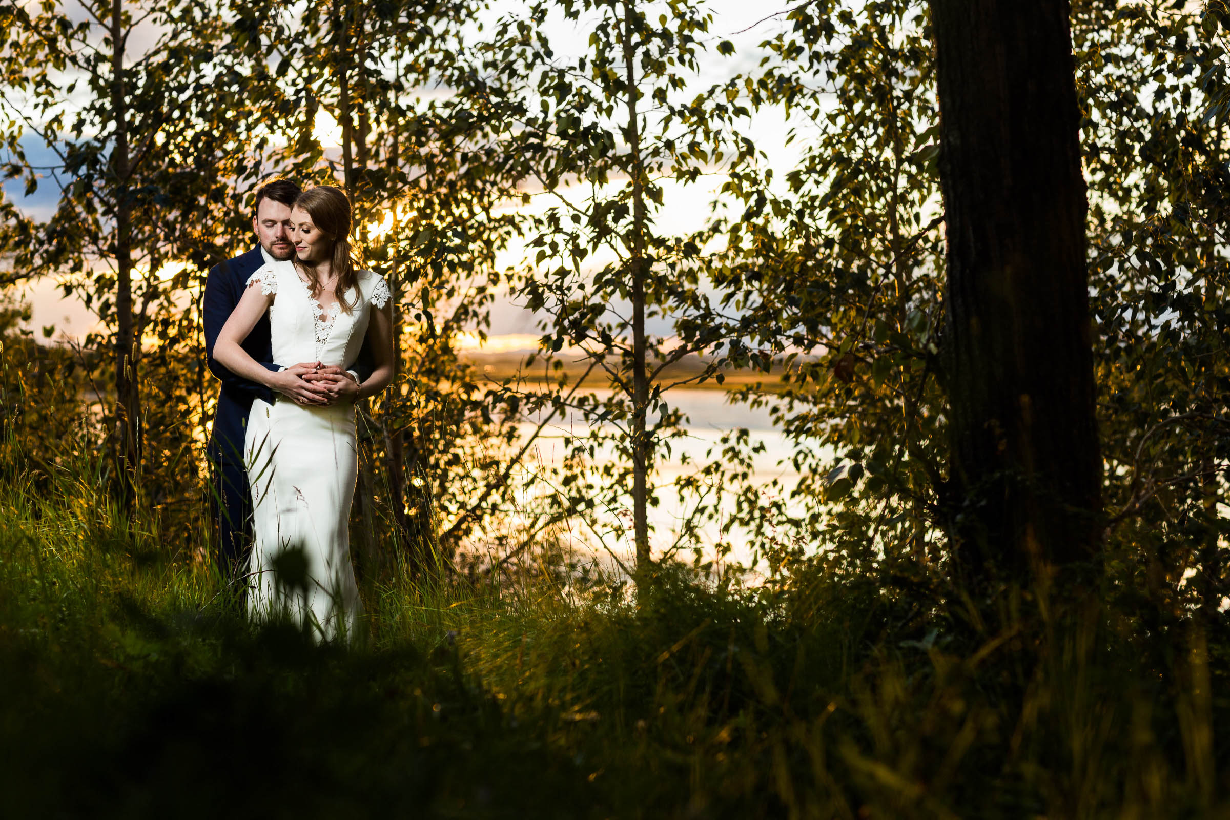 Bride and groom hugging in forest during sunset golden hour